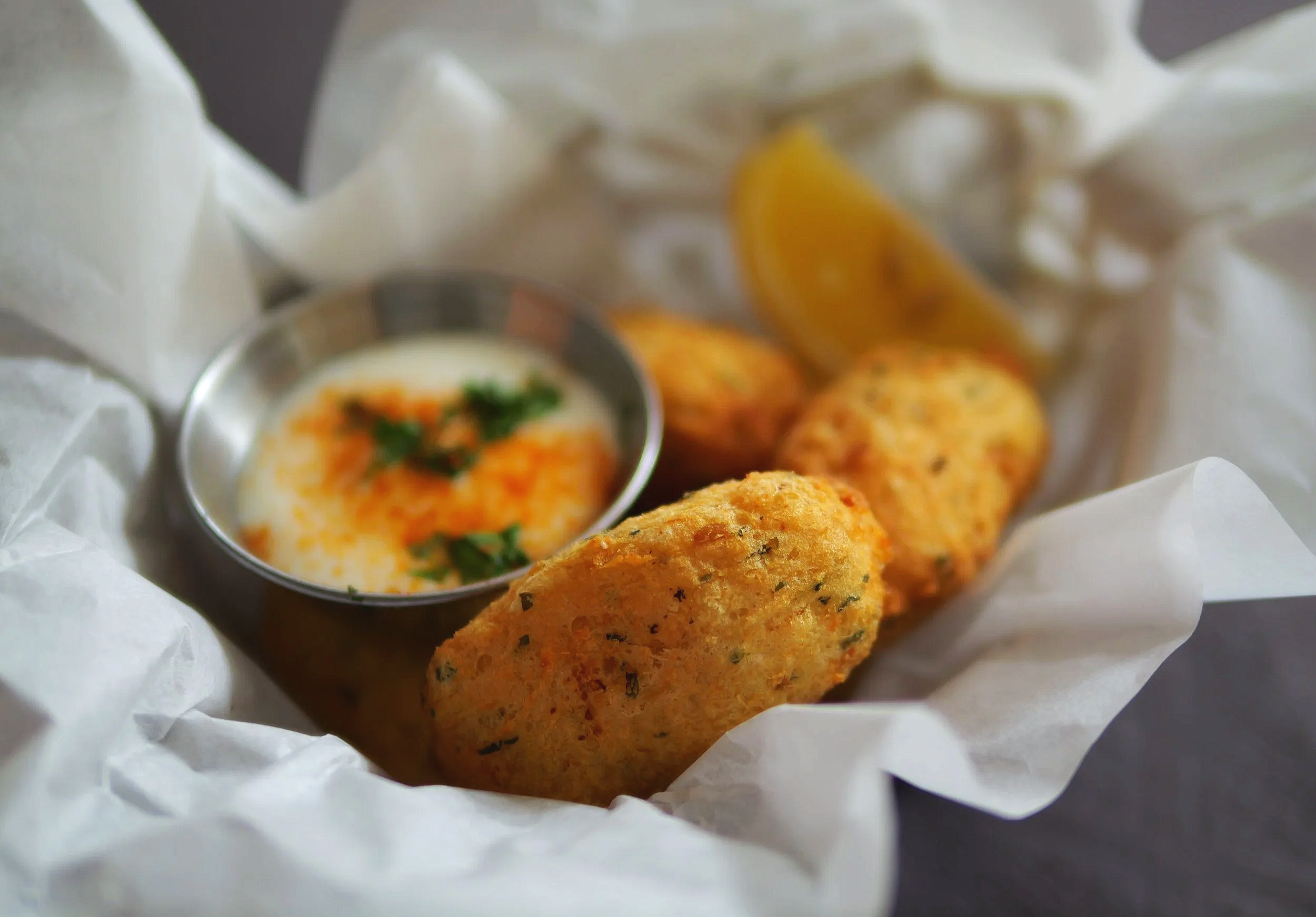 croquette de poissons dorées, servies avec une sauce, dans un panier en papier, Tapas