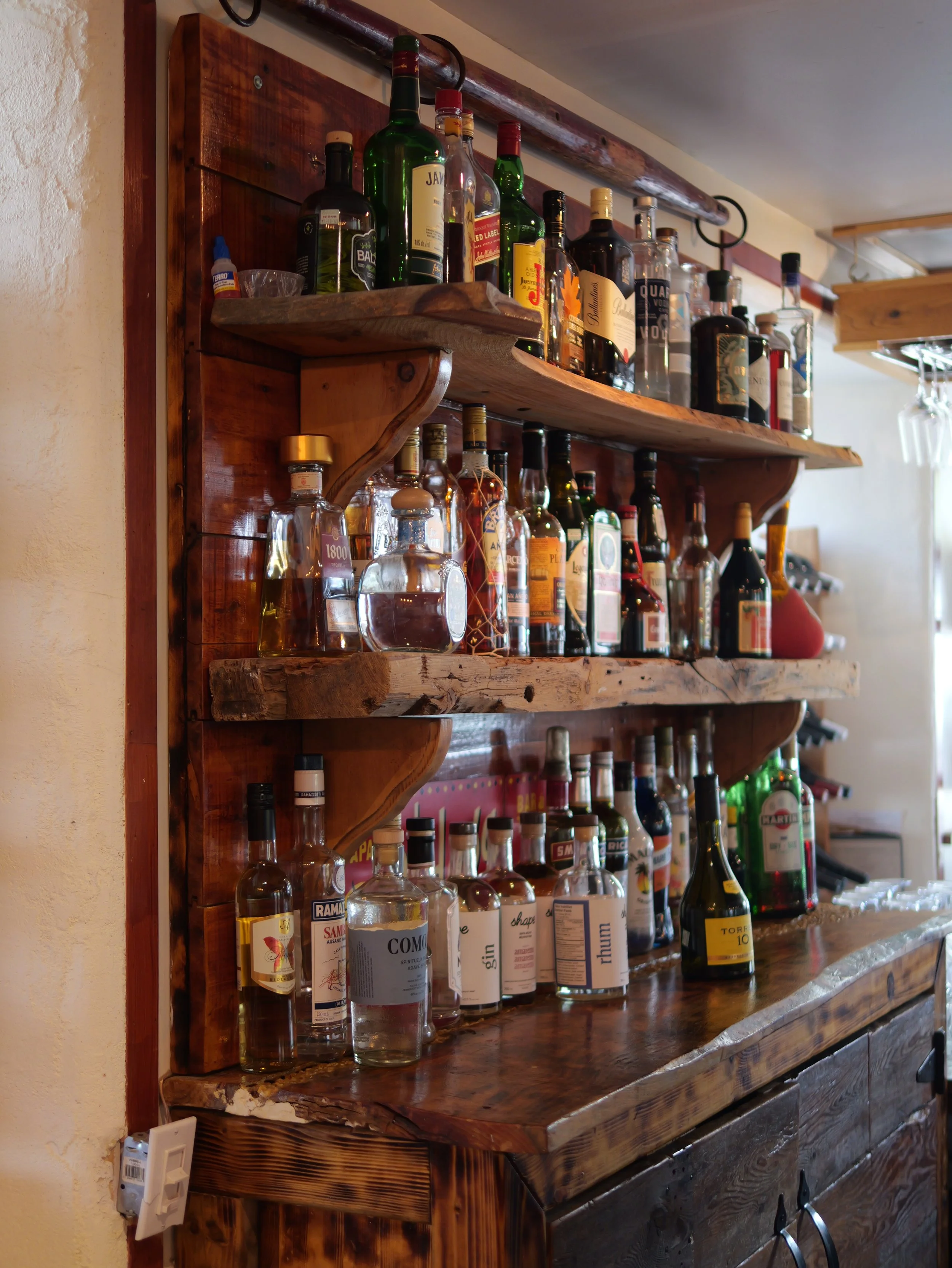 Étagère en bois avec diverses bouteilles d'alcool, y compris des spiritueux, dans un bar ou un restaurant en intérieur.