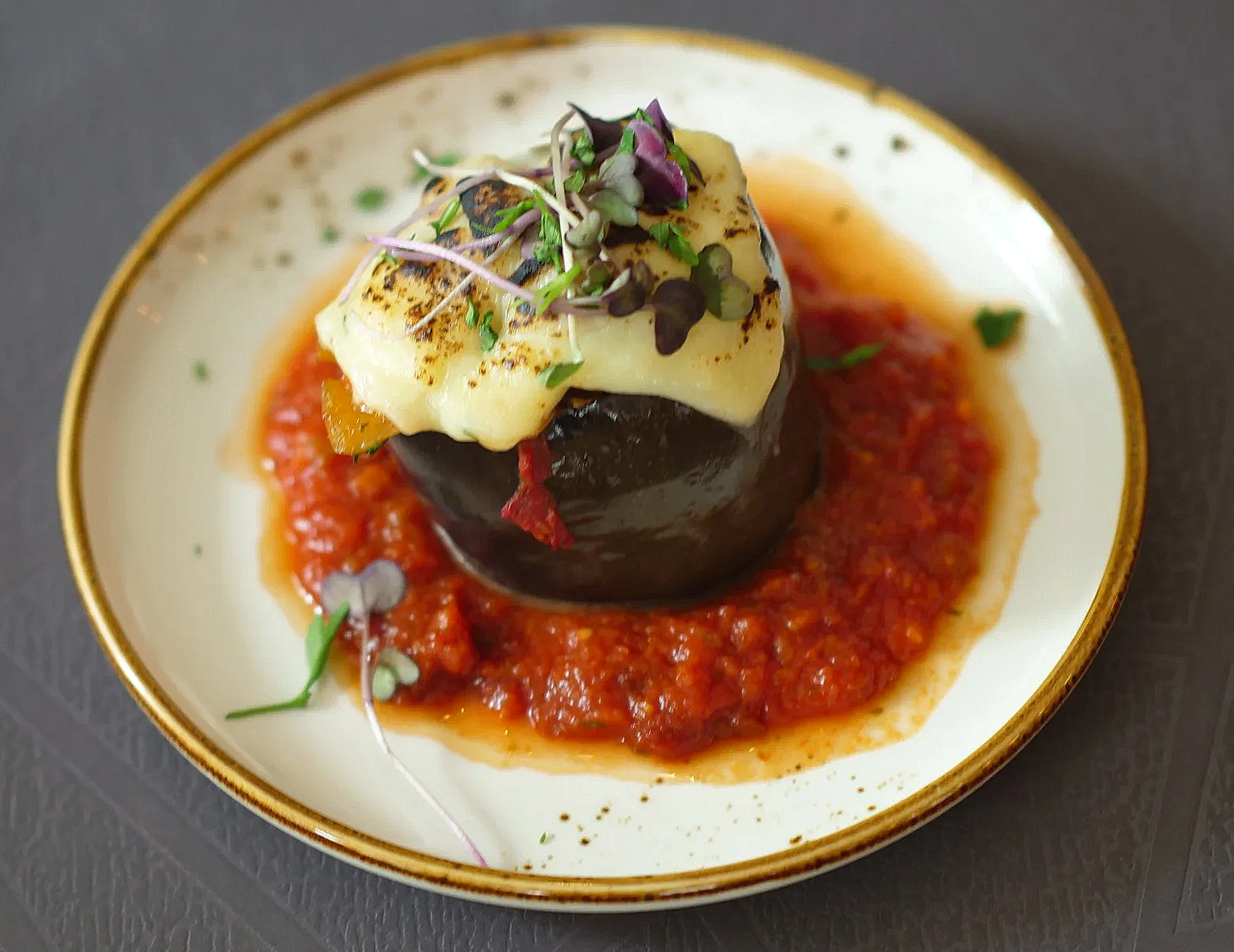 Plat de légumes farcis avec sauce tomate, garniture de microgreens et fromage grillé, servi sur une assiette blanche à bord doré.