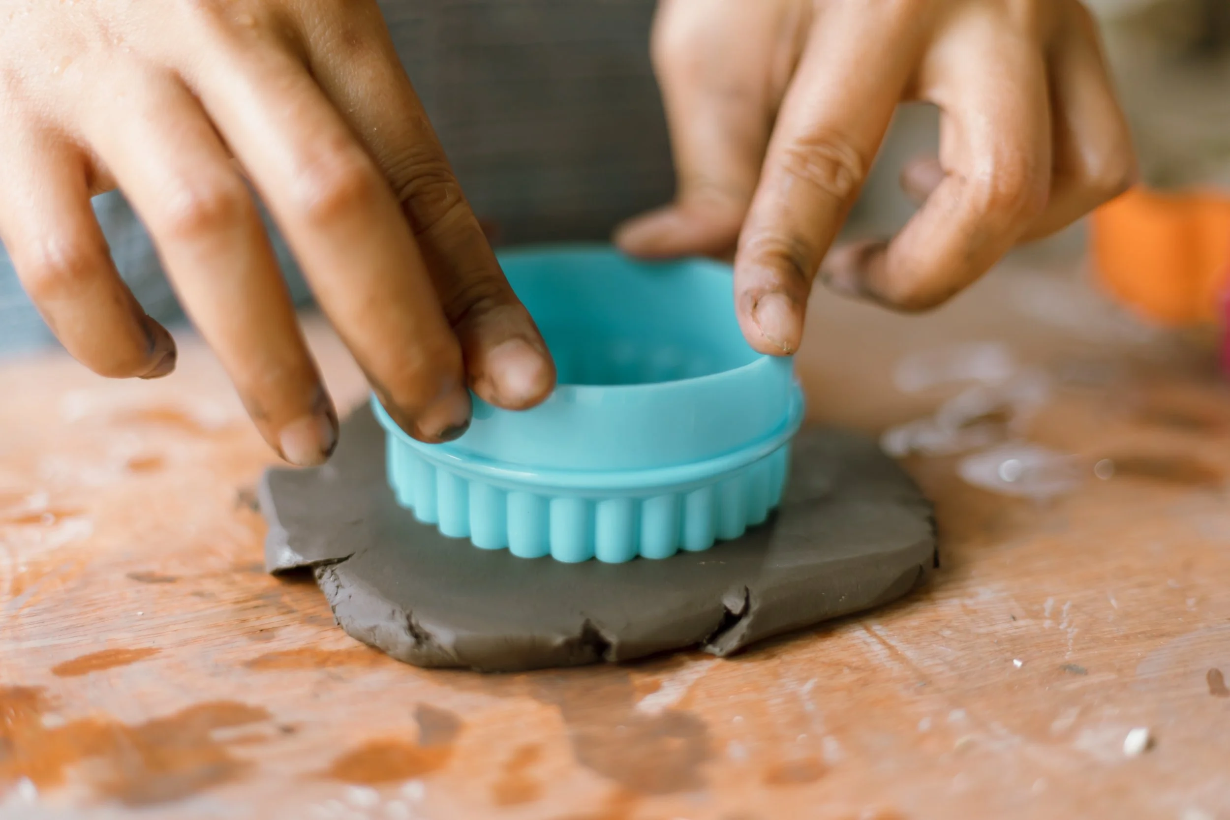 Close-up of hands pressing dough into a teal silicone mold on a wooden surface.