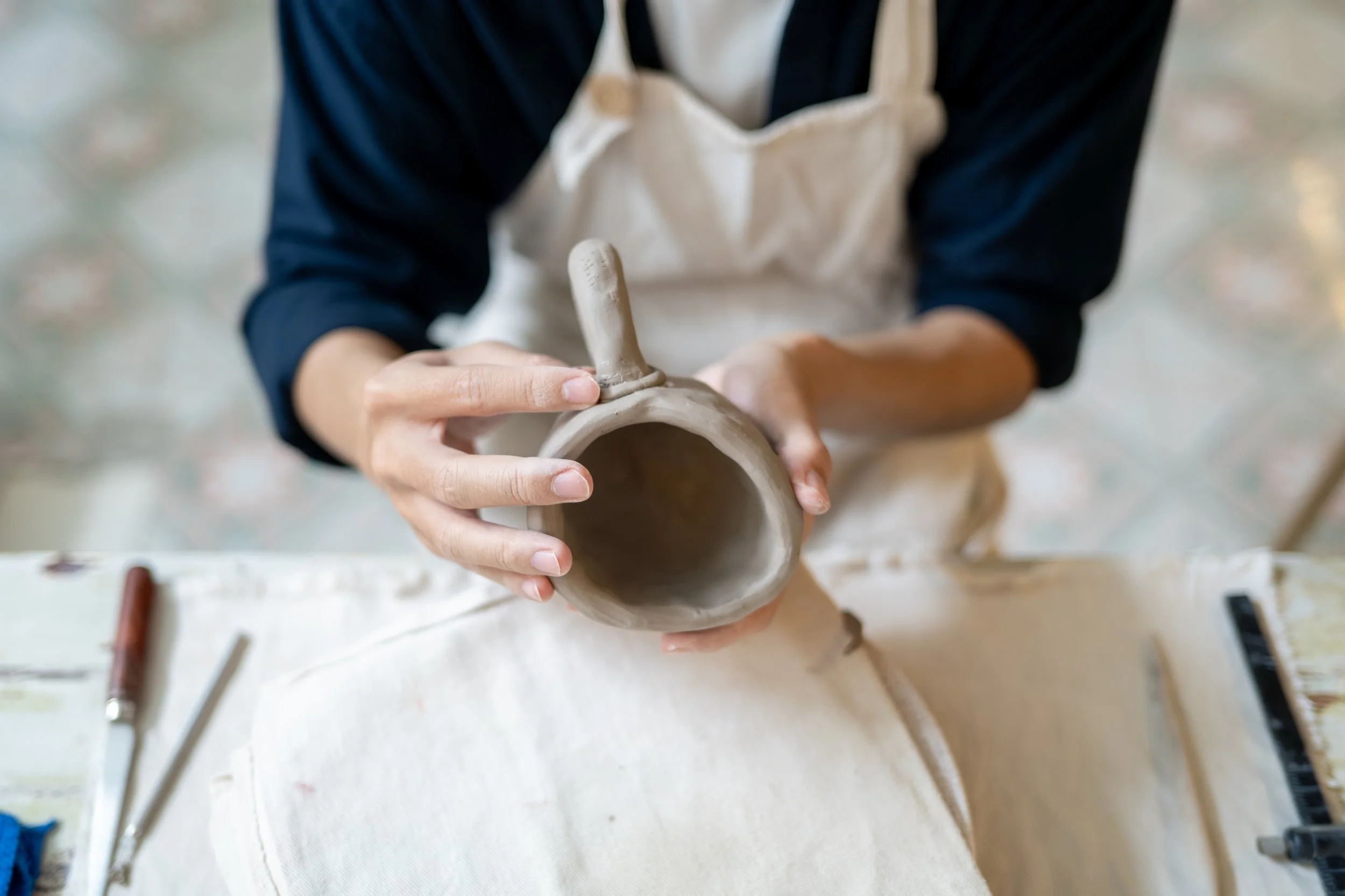 Person shaping clay on a pottery wheel in a workshop.
