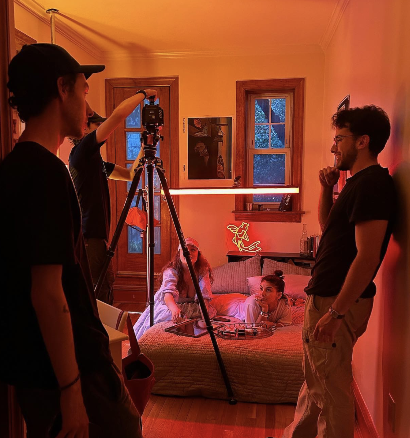 People filming a woman and a girl in a room with warm lighting, neon sign, and wooden accents.