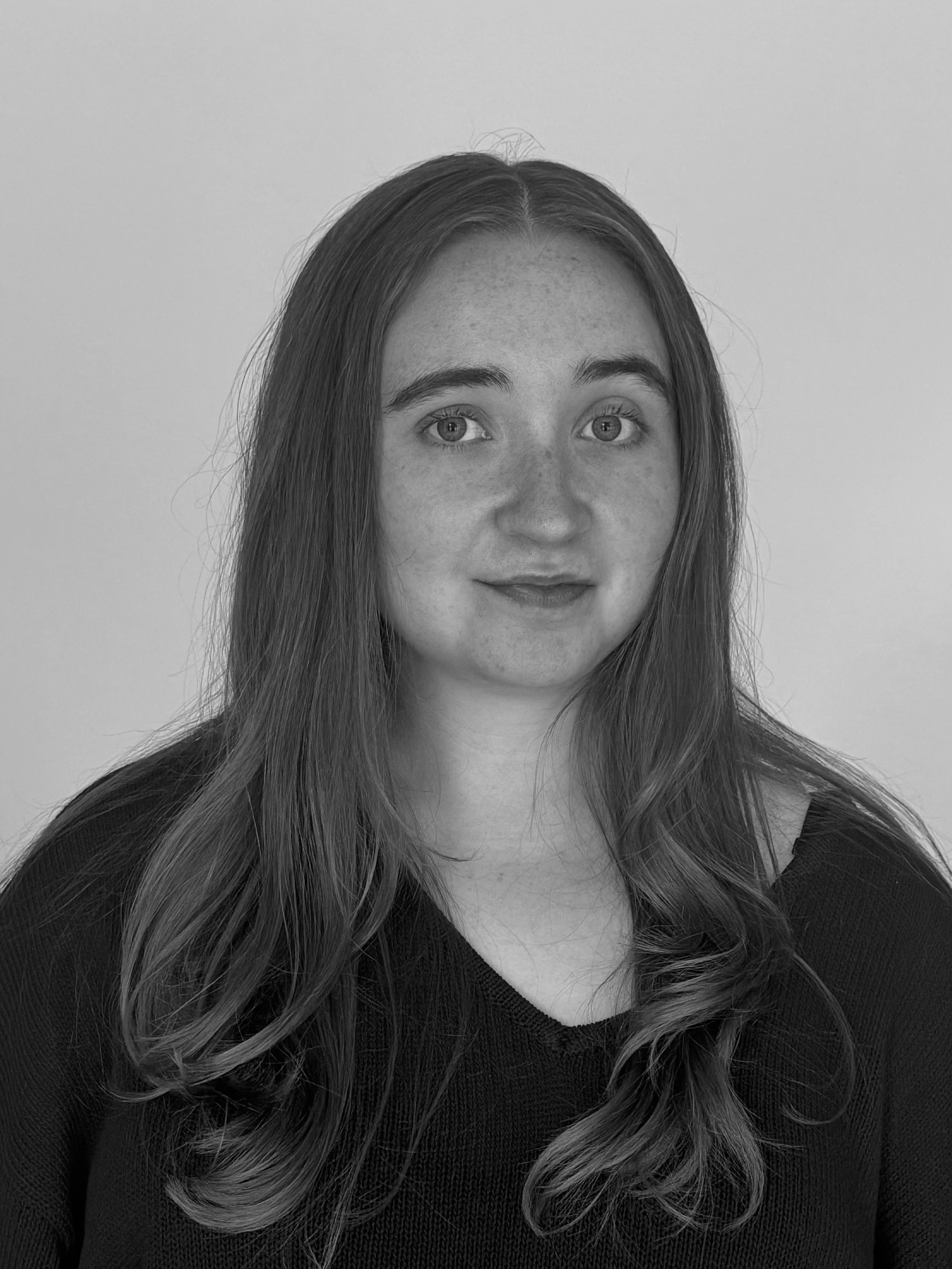 Black and white portrait of a young woman with long wavy hair, wearing a dark top, smiling slightly.