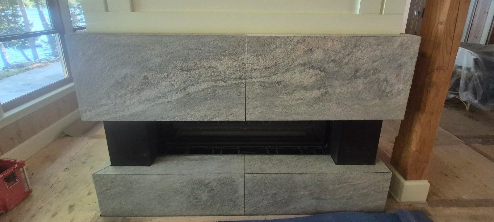A modern fireplace with a gray stone surround and a rectangular opening, situated against a wall inside a house.