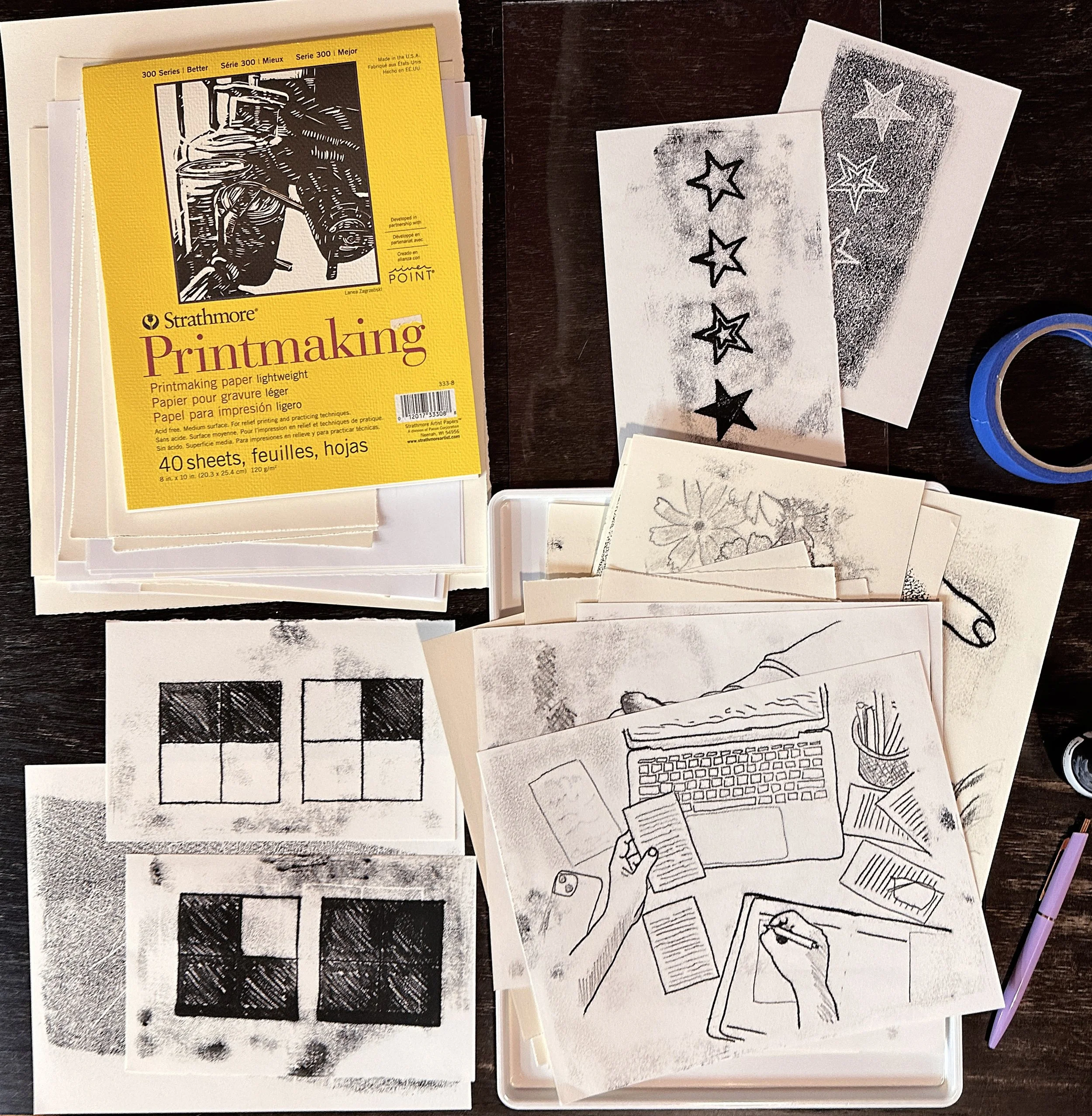 Art supplies including printmaking paper, rubber stamps with star patterns, and various sketches and drawings on paper.