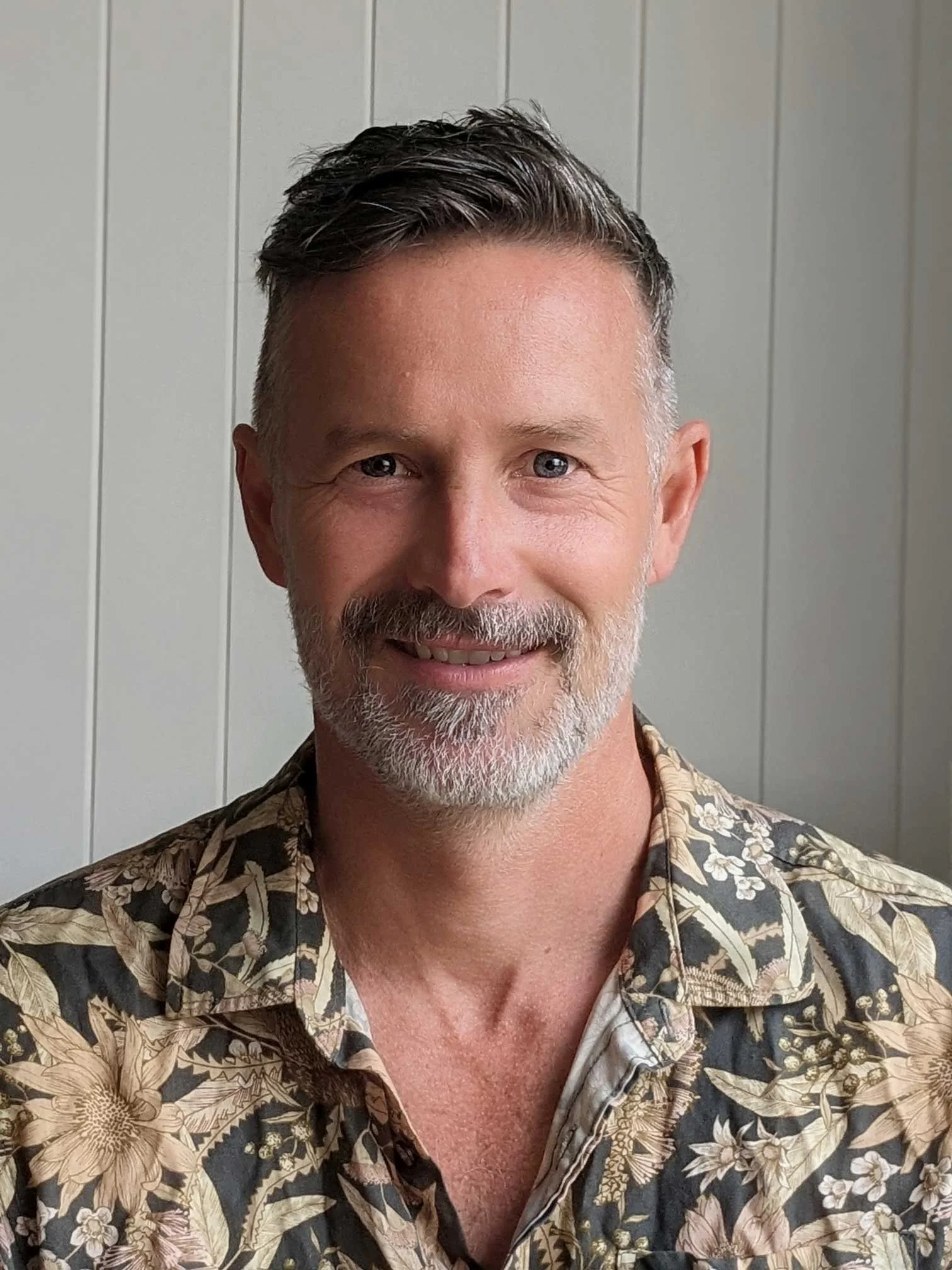 Nick Lines, wearing a floral-patterned shirt, standing in front of a plain wall with vertical panels.