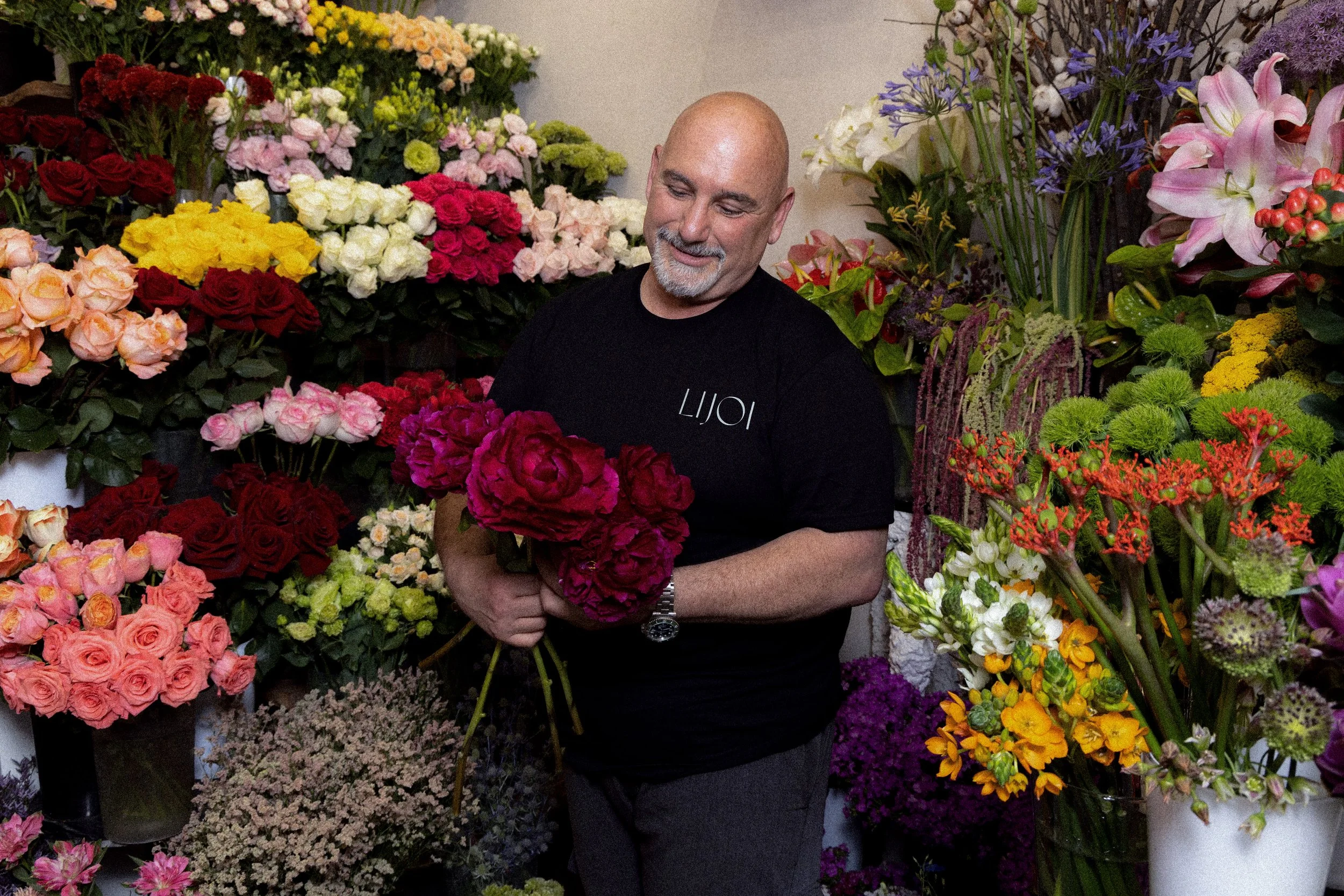 Uomo in una flower shop circondato da fiori di vari colori, mentre tiene un grande mazzo di rose rosse.