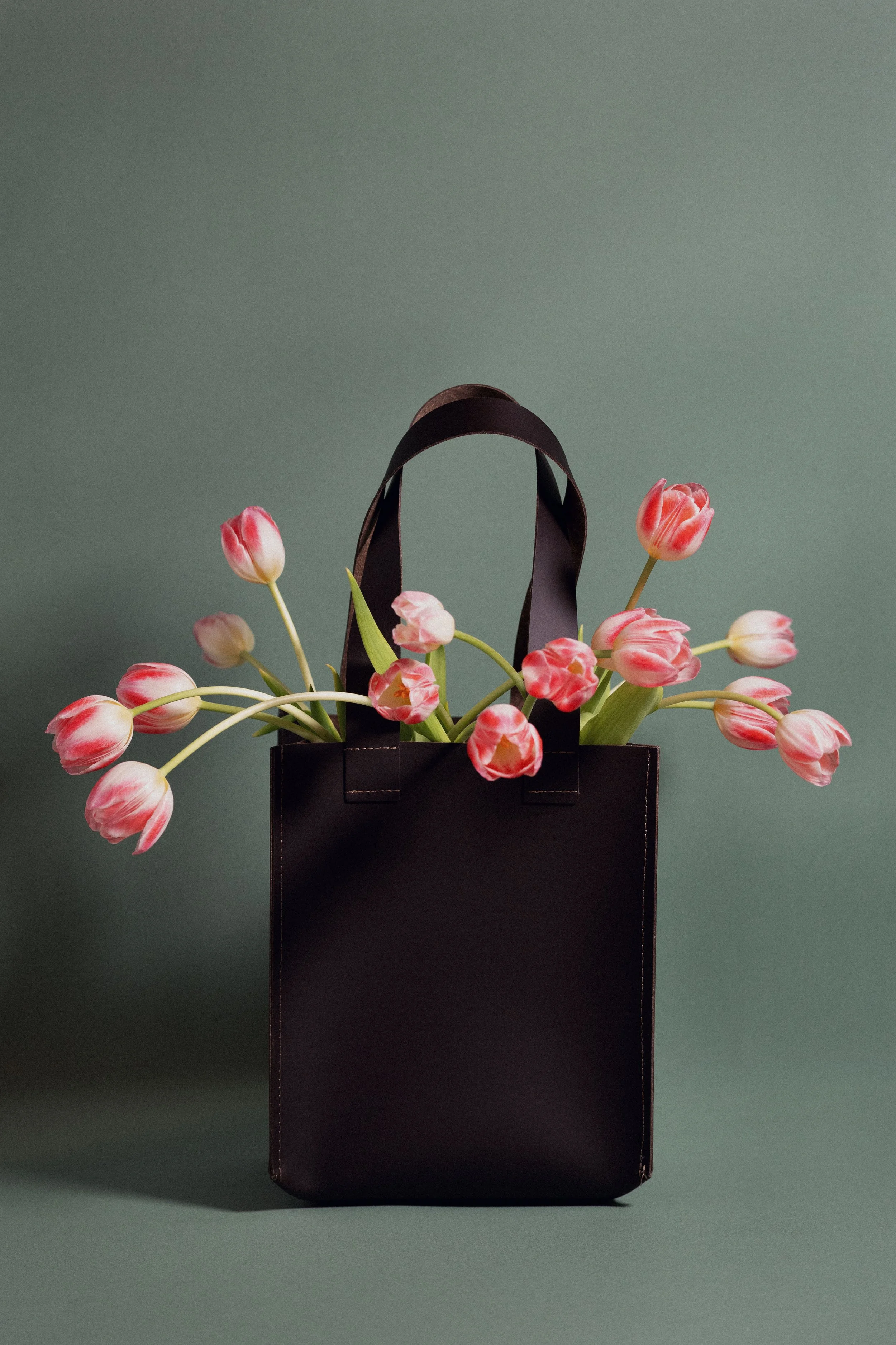 Borsa nera con manici, riempita di tulipani rosa, su sfondo verde ../../../