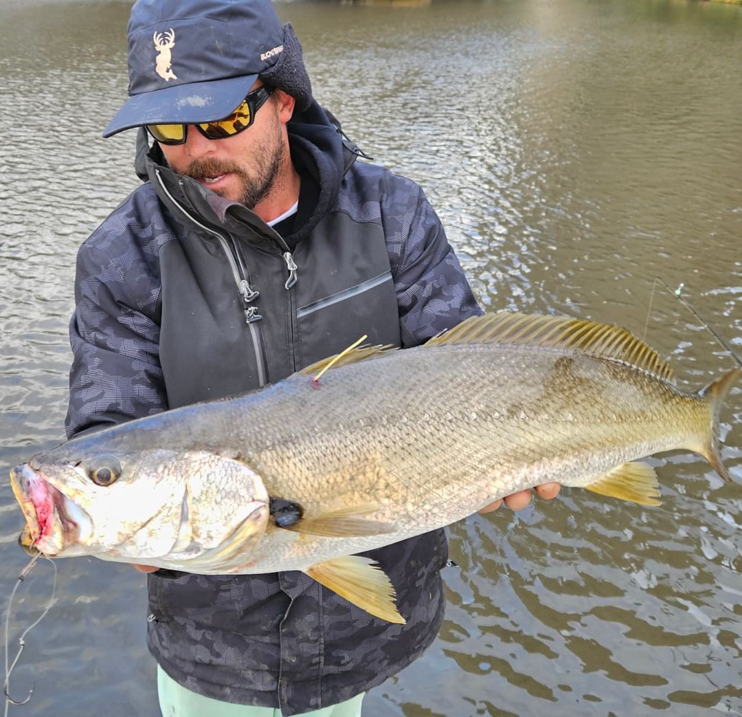 A man in fishing gear holding a large fish over a body of water.