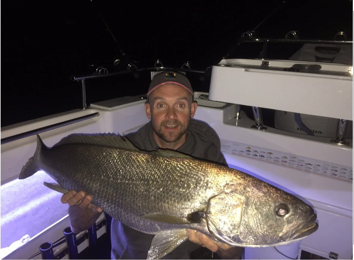 Man holding a large fish on a boat at night