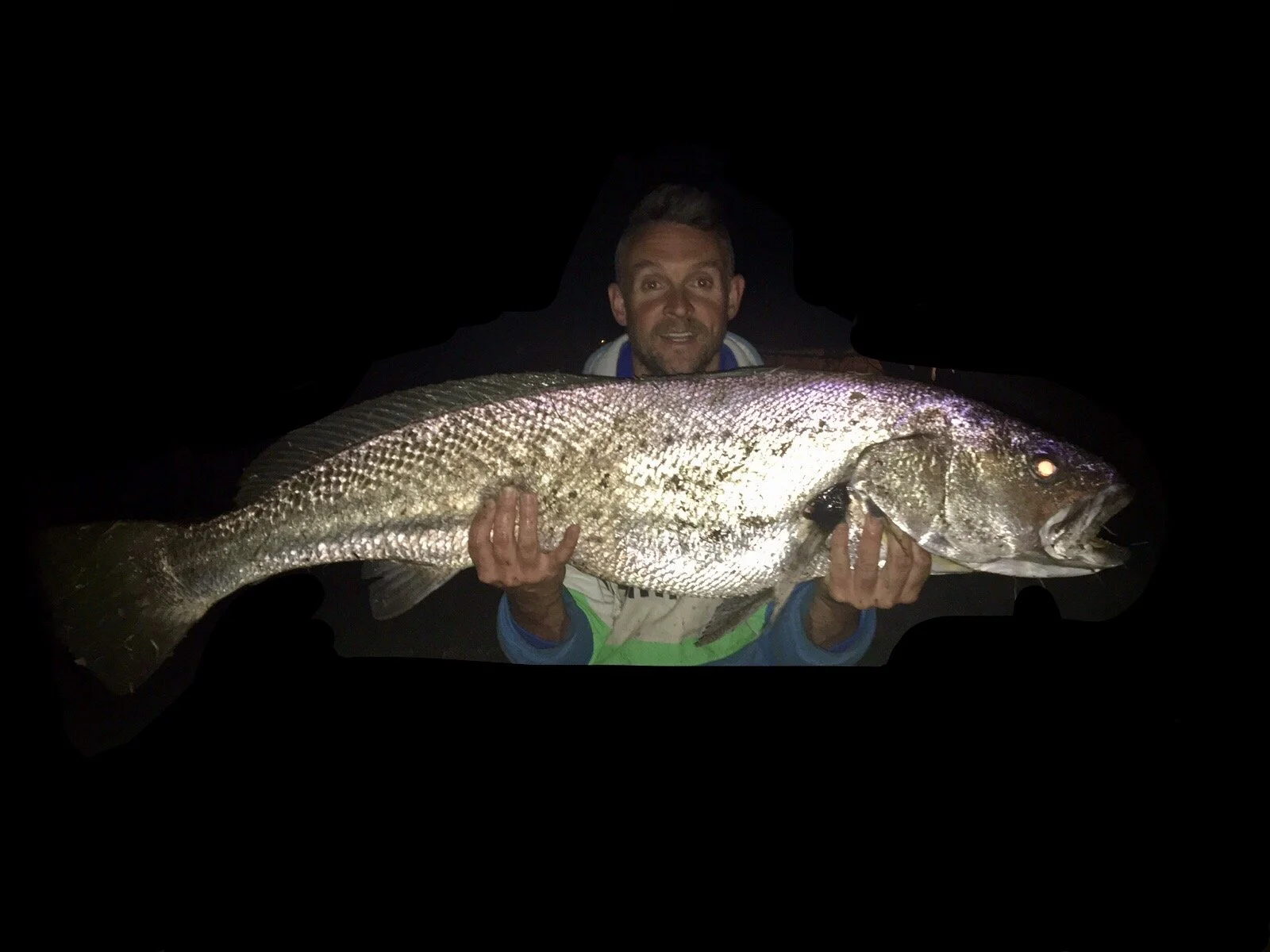 Man holding a large fish at night, with a dark background.