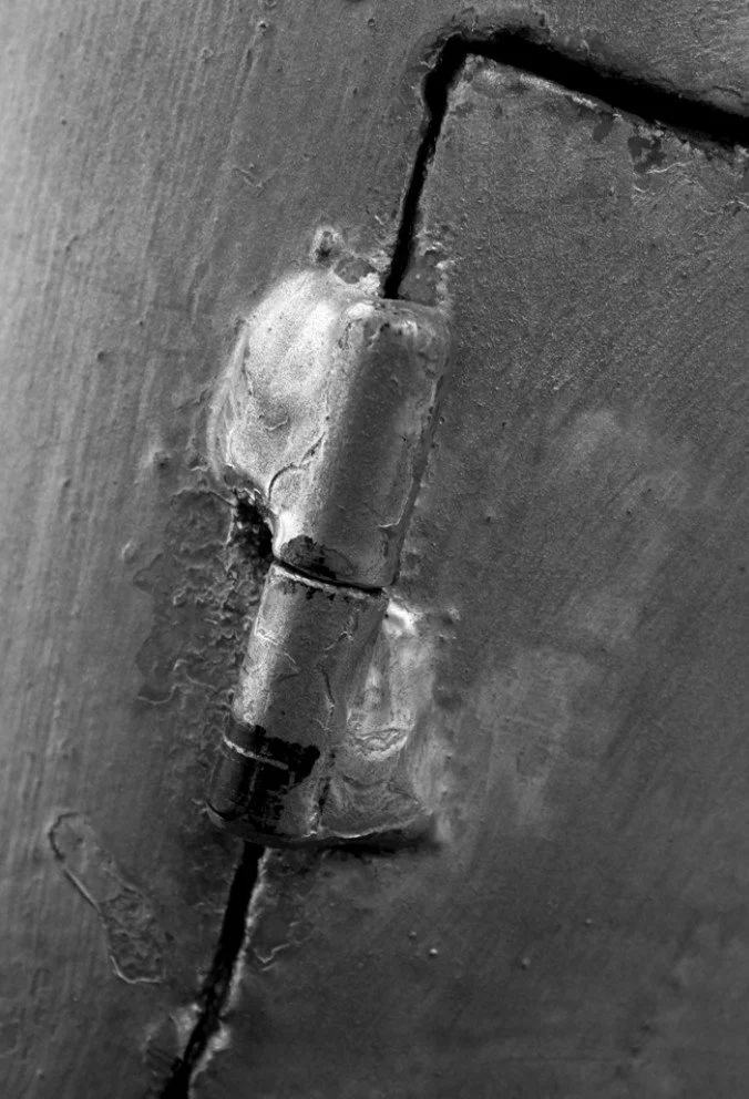 Every threshold carries the promise of another side. Yet the hinge remembers that every opening is already inhabited by closure. Rust is not decay but writing—the slow inscription of time upon metal. What appears immobile continues to defer its desti