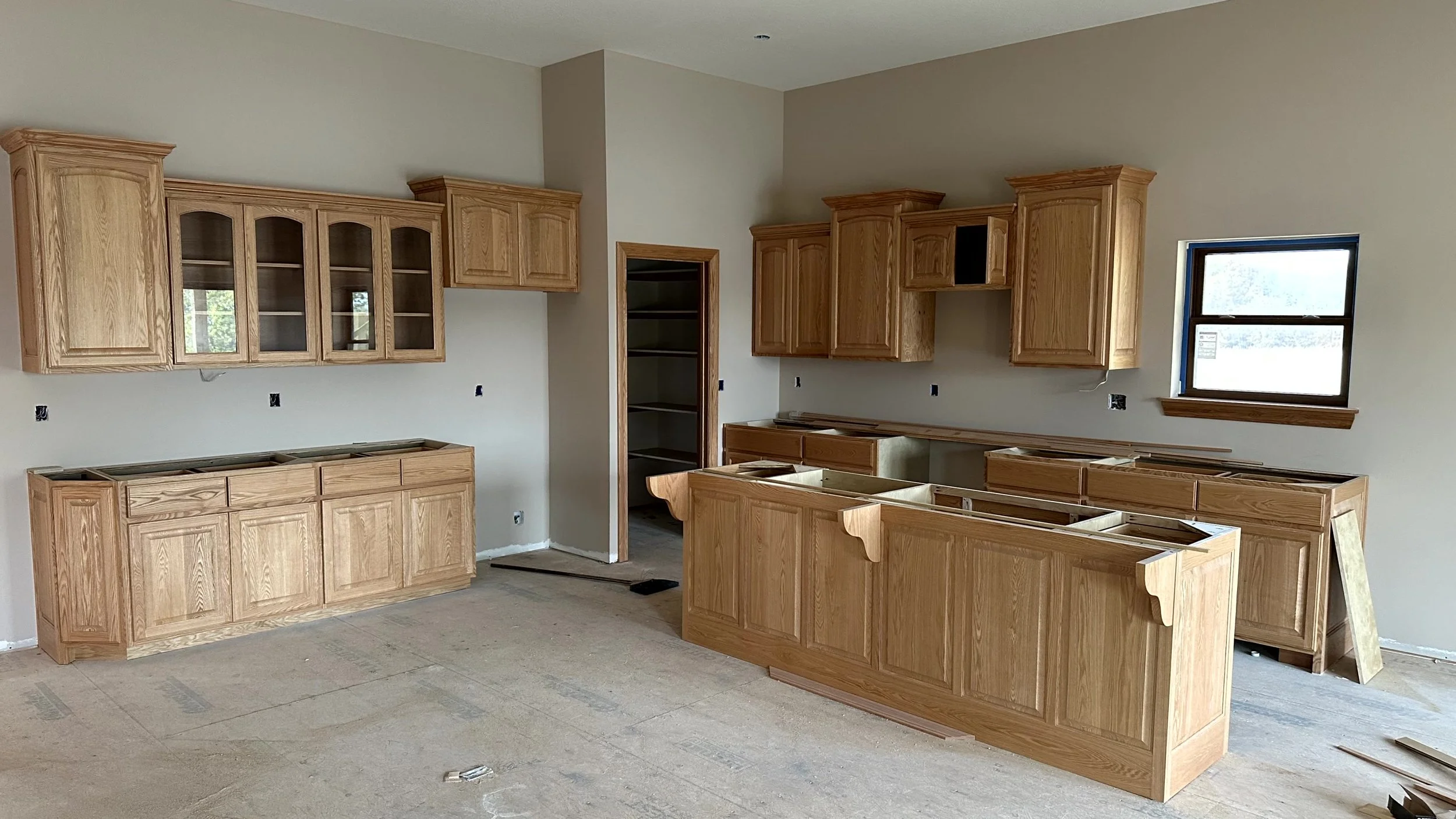 Kitchen under construction with wooden cabinets, some open shelves, and a window on the right.