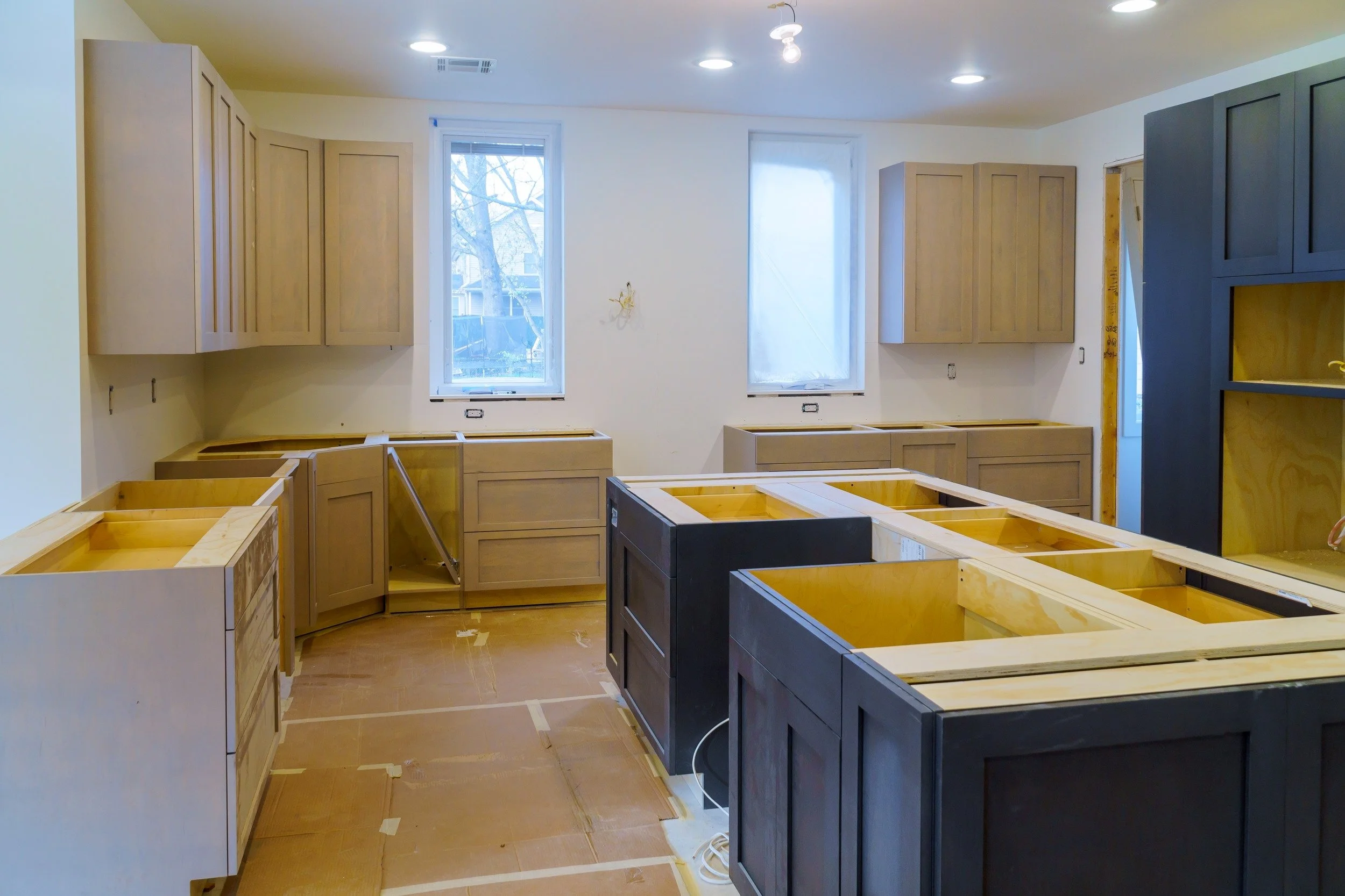 Kitchen under construction with light wood and dark cabinets, windows, and unfinished counters.