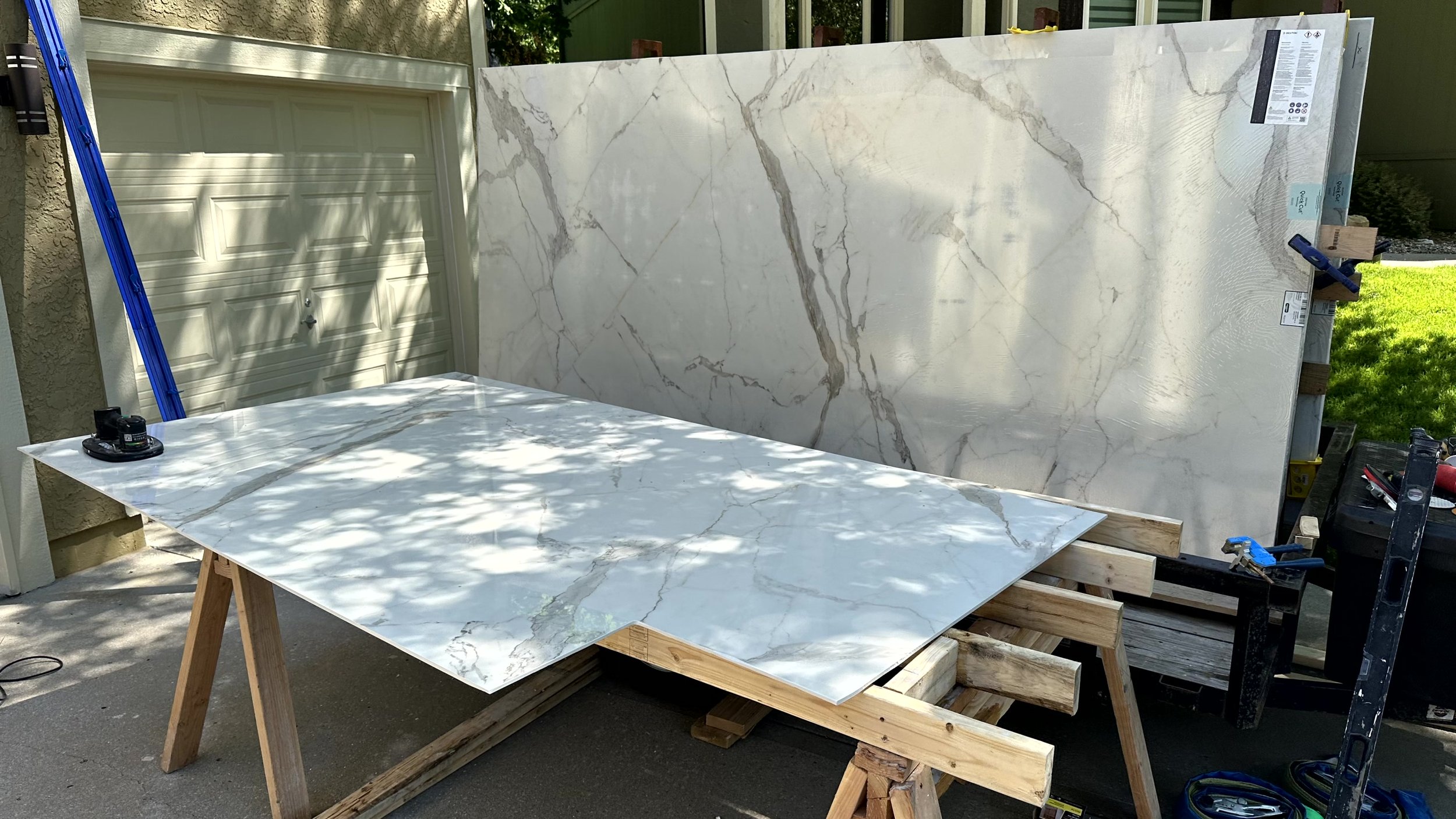 Large slab of white marble with gray and brown veining resting on a wooden work table outside.