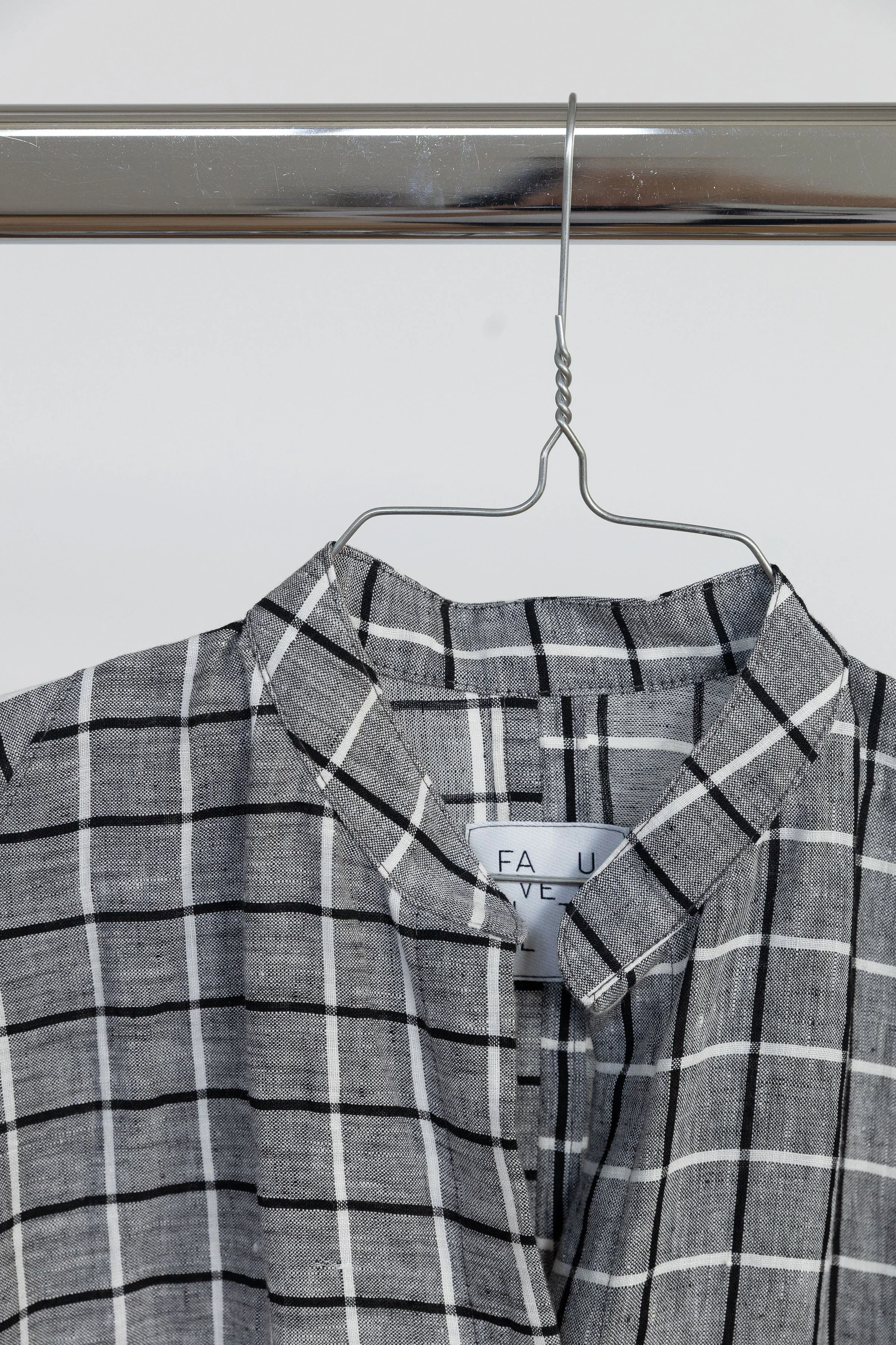 Chemise à carreaux noir et blanc suspendue à un cintre métallique.