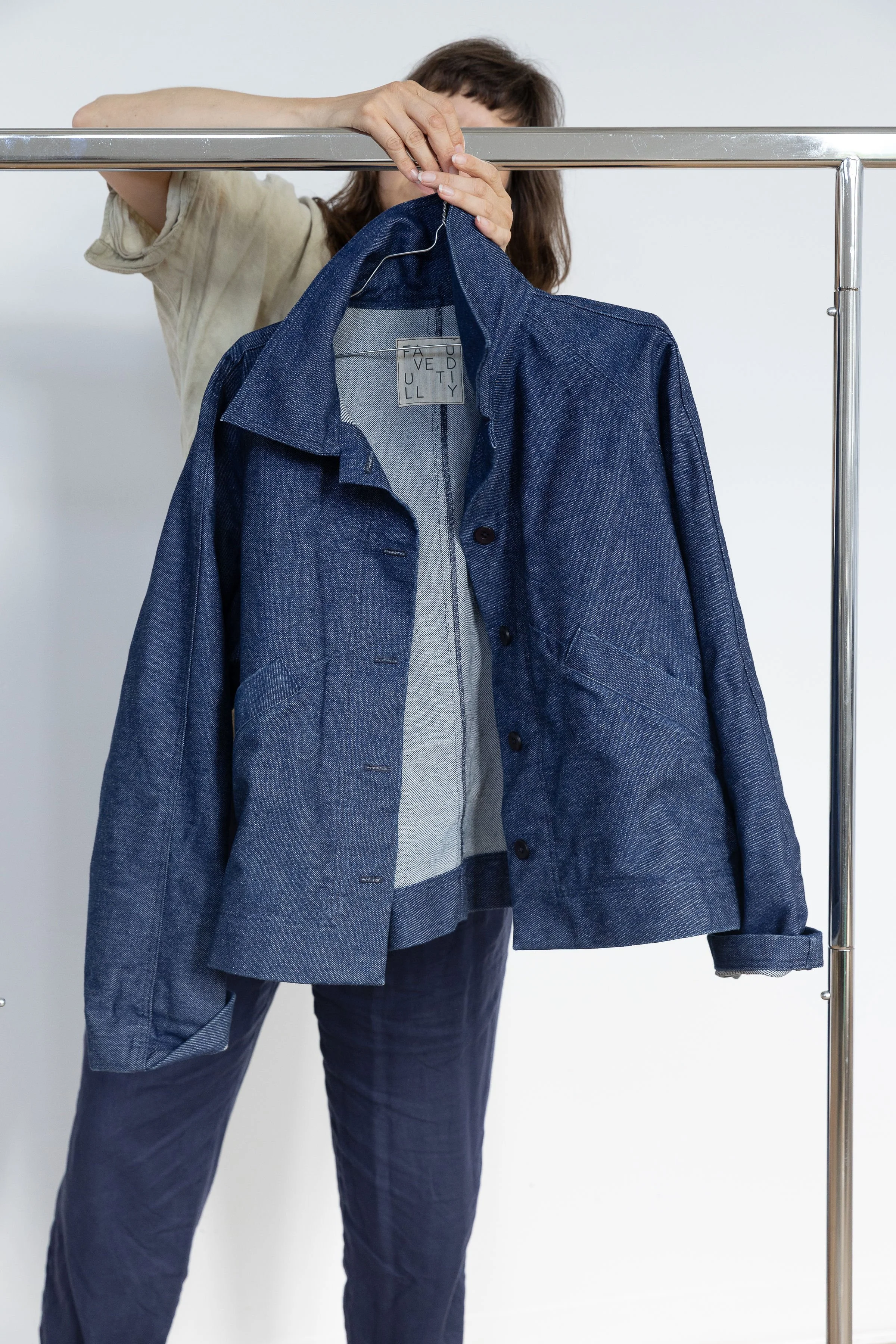 Une personne tenant une veste en denim bleu sur un portemanteau, avec un fond blanc.