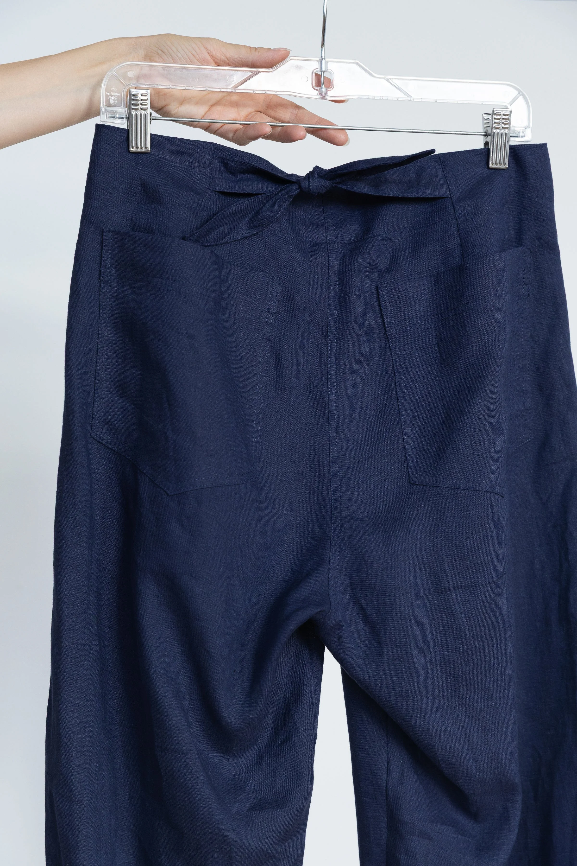 Une paire de pantalons bleus avec une taille nouée, suspendus sur un cintre en plastique transparent.