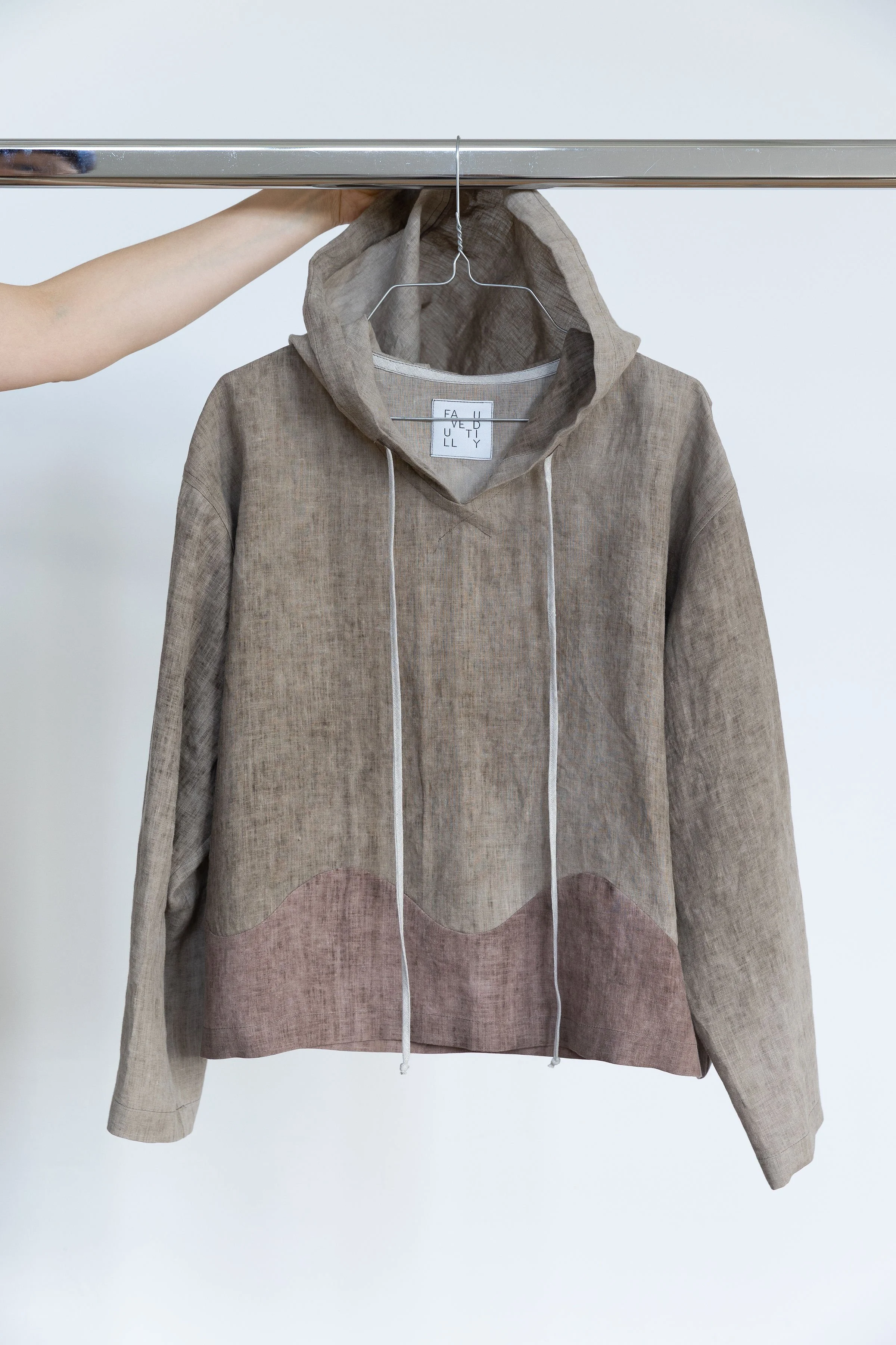 Veste en tissu beige avec un capuchon, suspendue sur un cintre, image prise en gros plan contre un fond blanc.