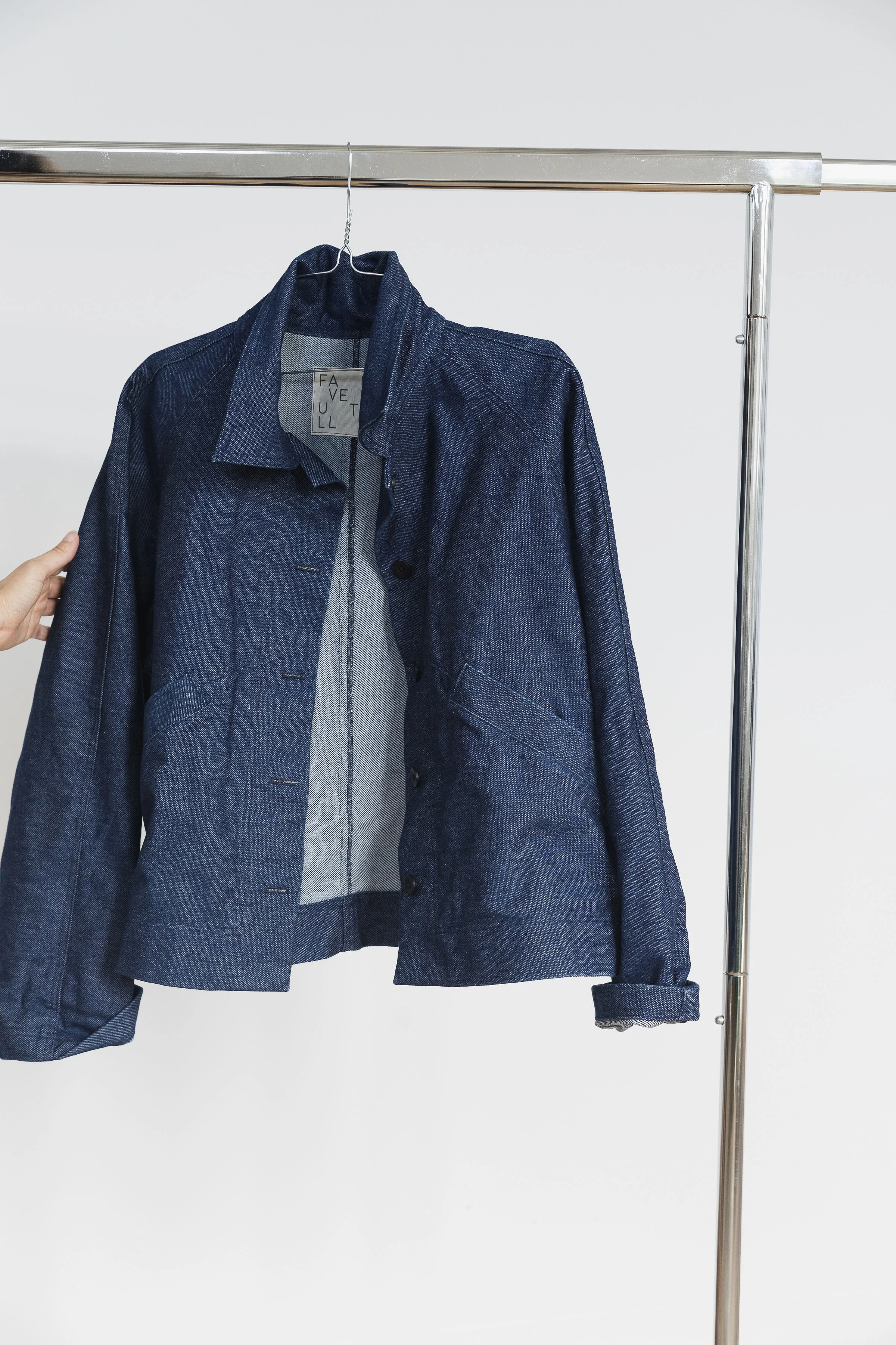 Une veste en jean bleu suspendue sur un portemanteau en métal dans un mur blanc.