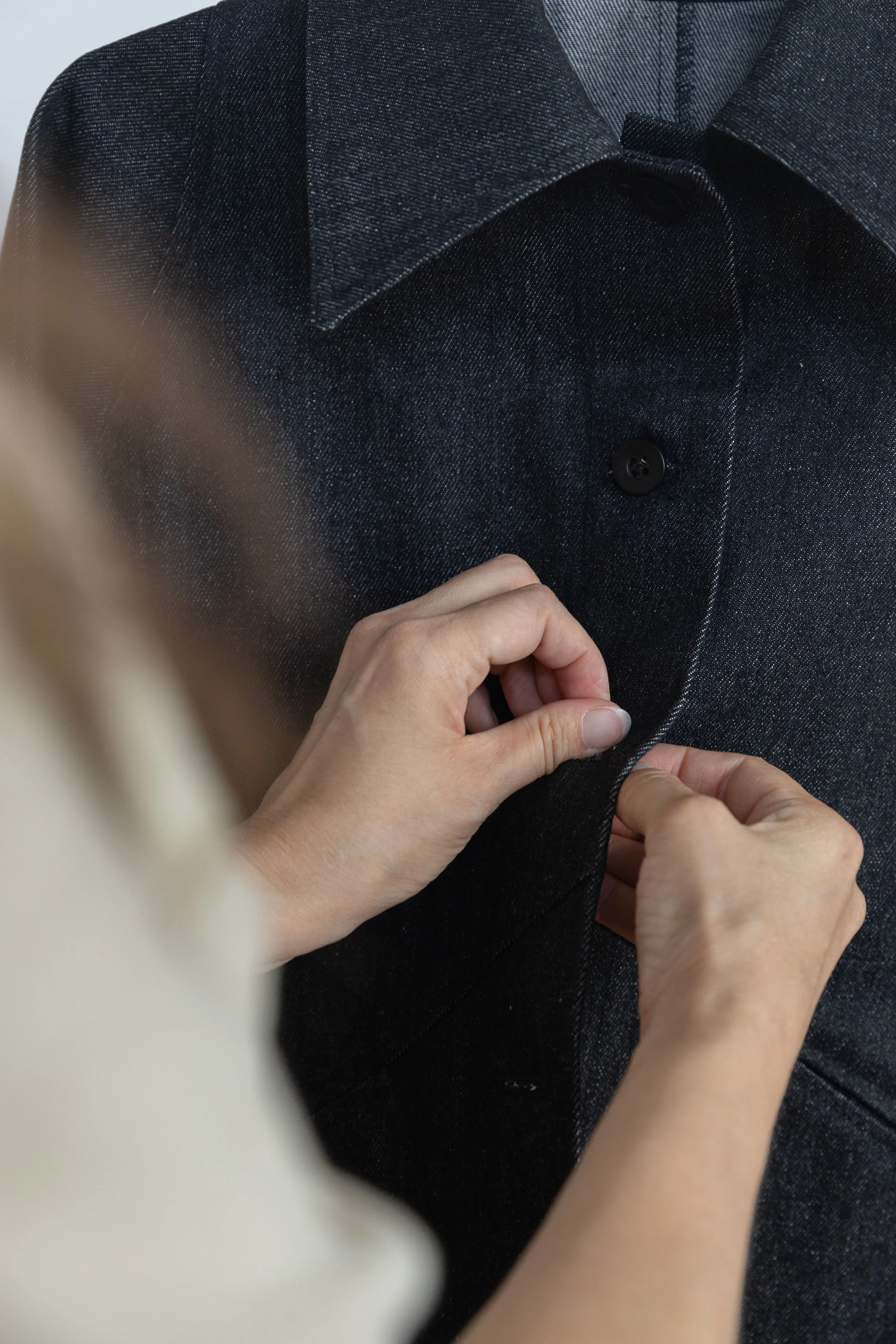 Une personne ajuste un bouton noir sur un manteau en tissu gris foncé.