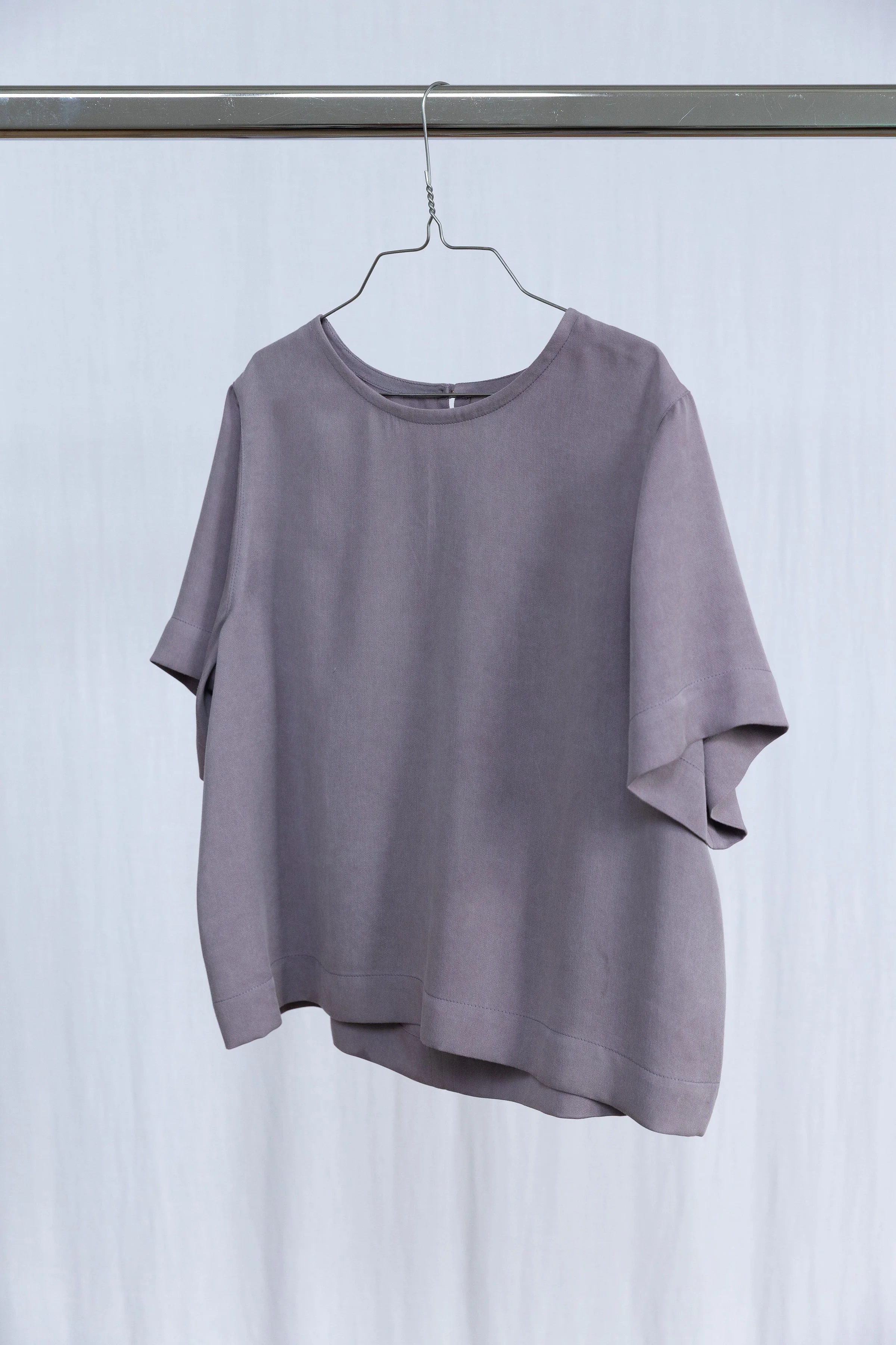 Une chemise grise suspendue sur un cintre métallique accroché à une barre.