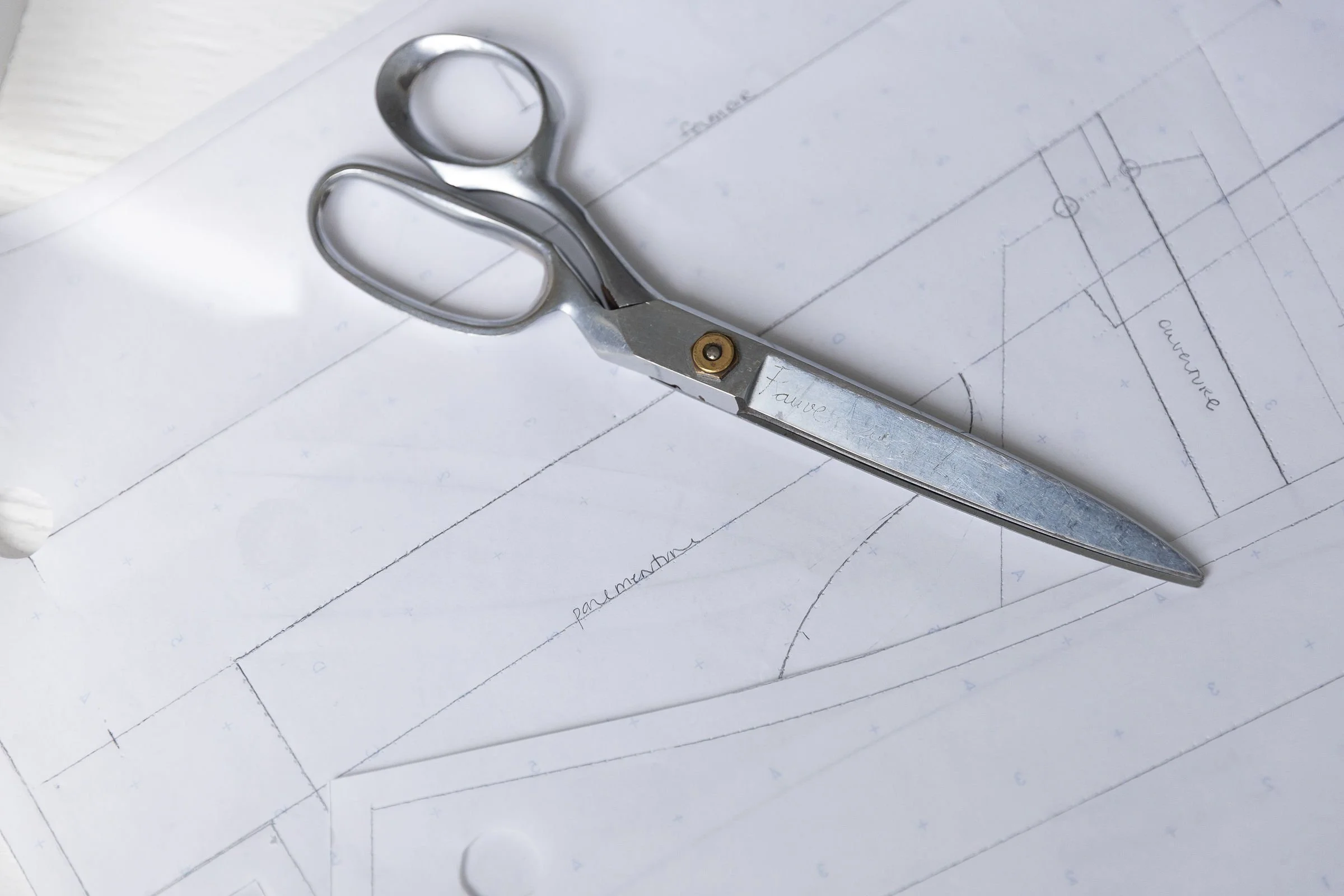 Une paire de ciseaux en métal repose sur des plans d'architecture ou de conception dessinés à la main.
