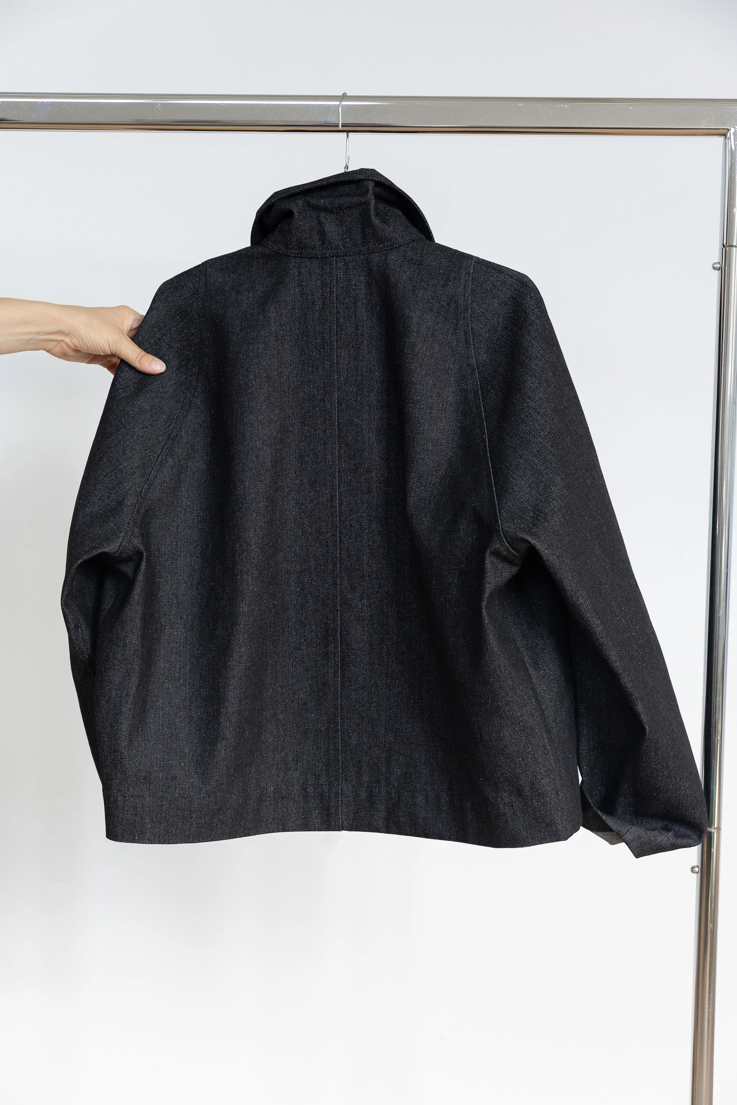 Veste noire suspendue à un portemanteau en métal, une main la tenant par l'épaule
