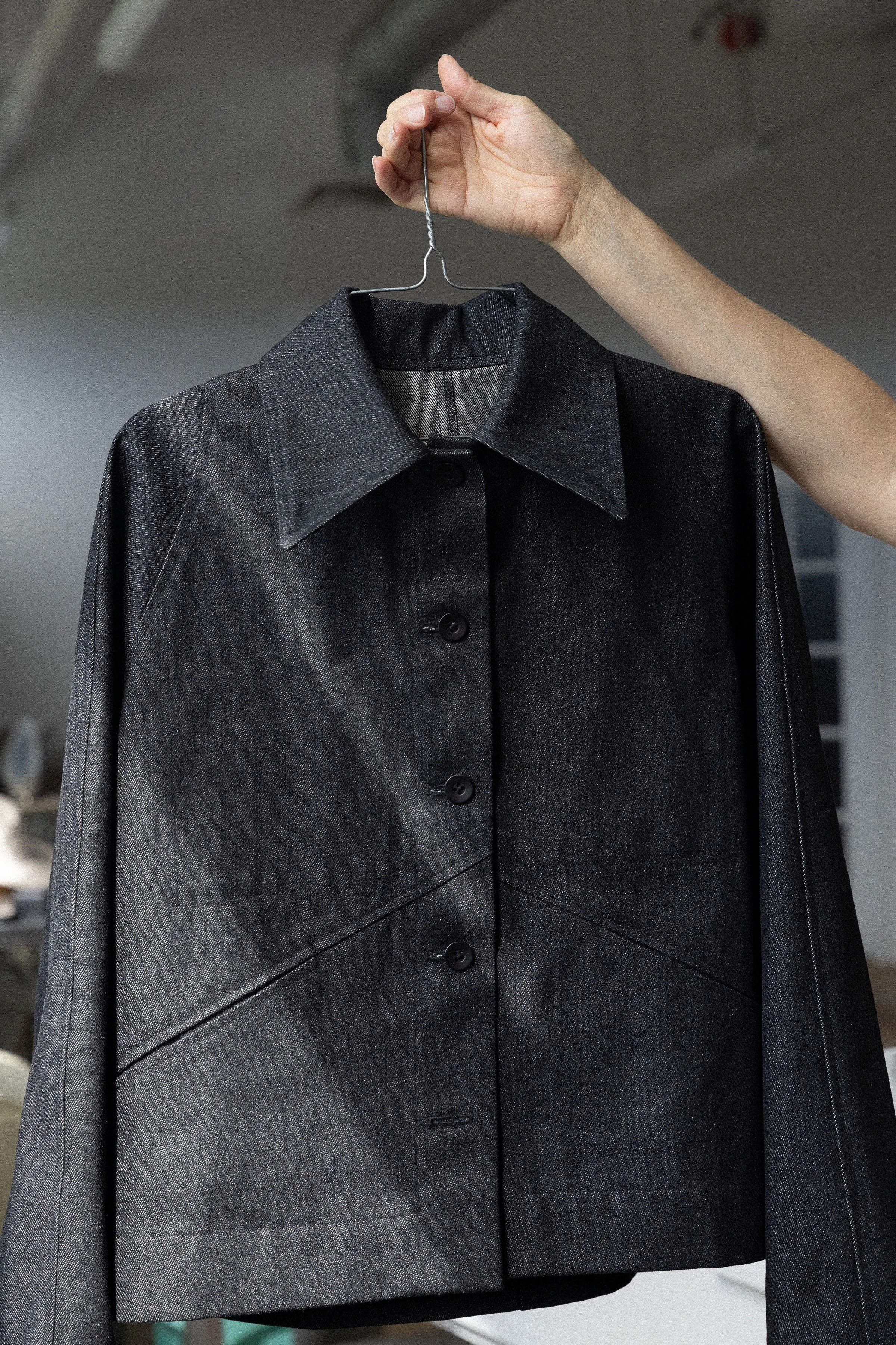 Veste noire en tissu texturé suspendue par une main.