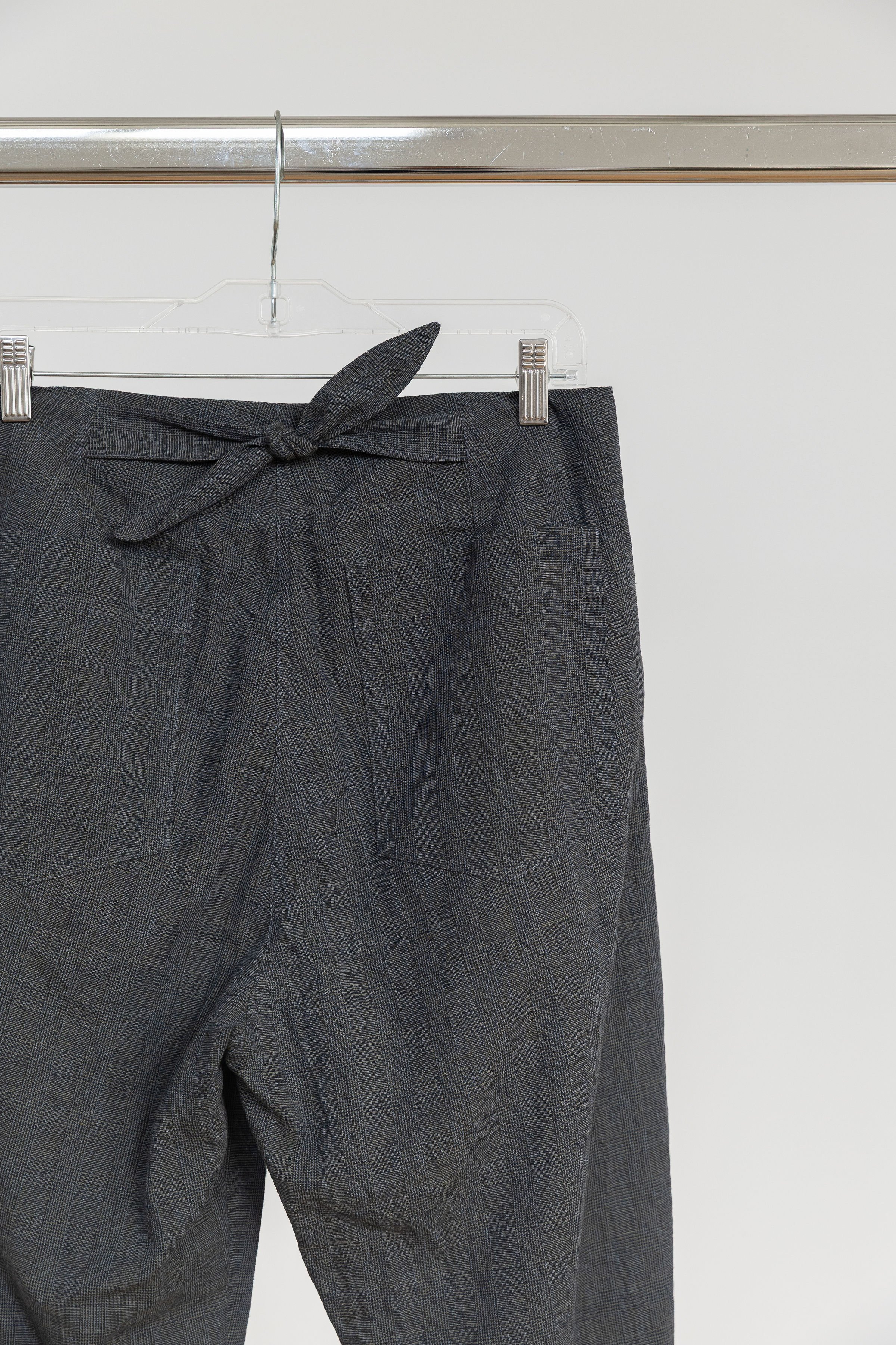 Pantalon gris à motif à carreaux avec ceinture nouée, suspendu à un cintre en plastique transparent.