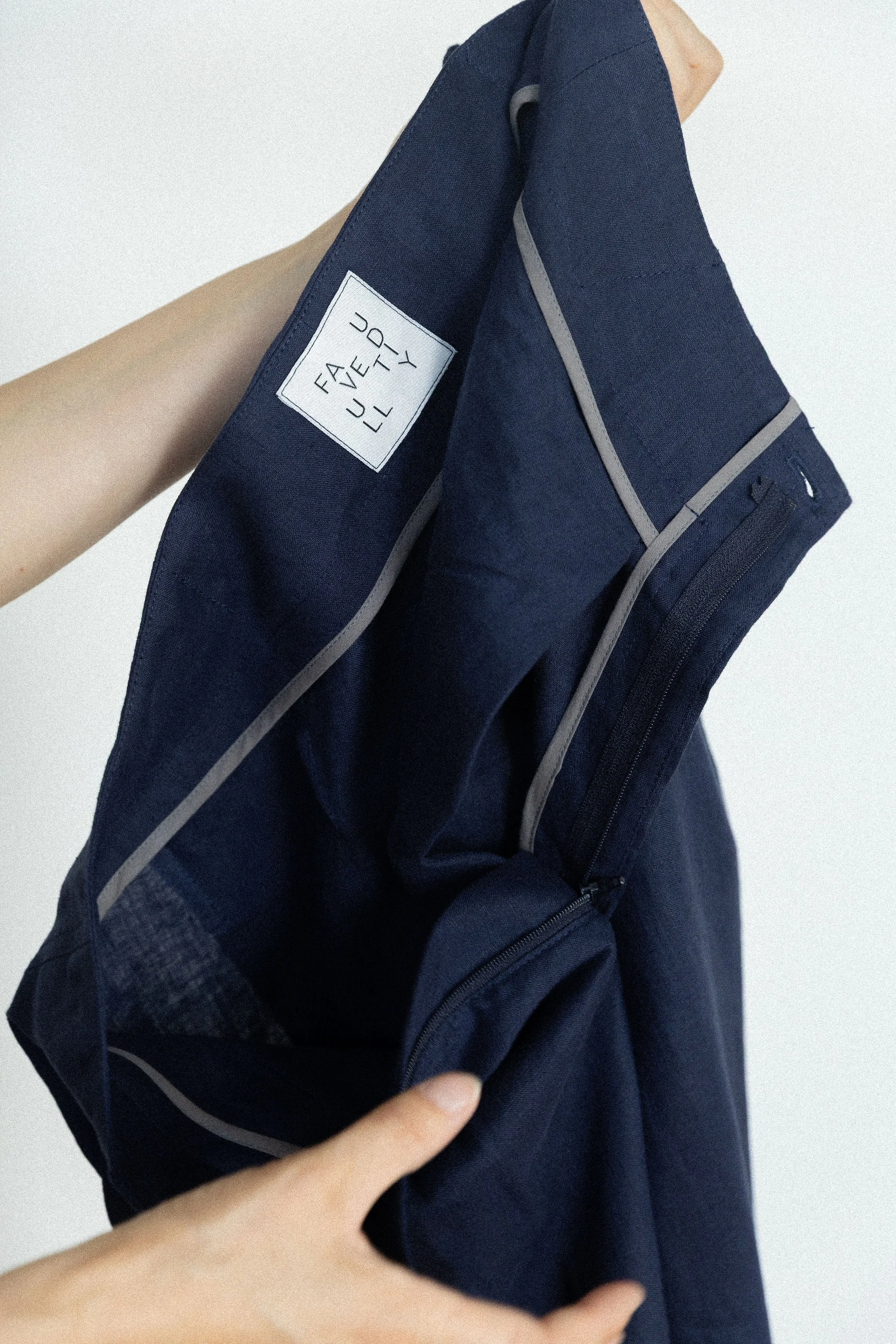 Une personne tient un sac à dos bleu marine avec une étiquette blanche affichant 'FAIRY' en noir, contre un fond blanc.