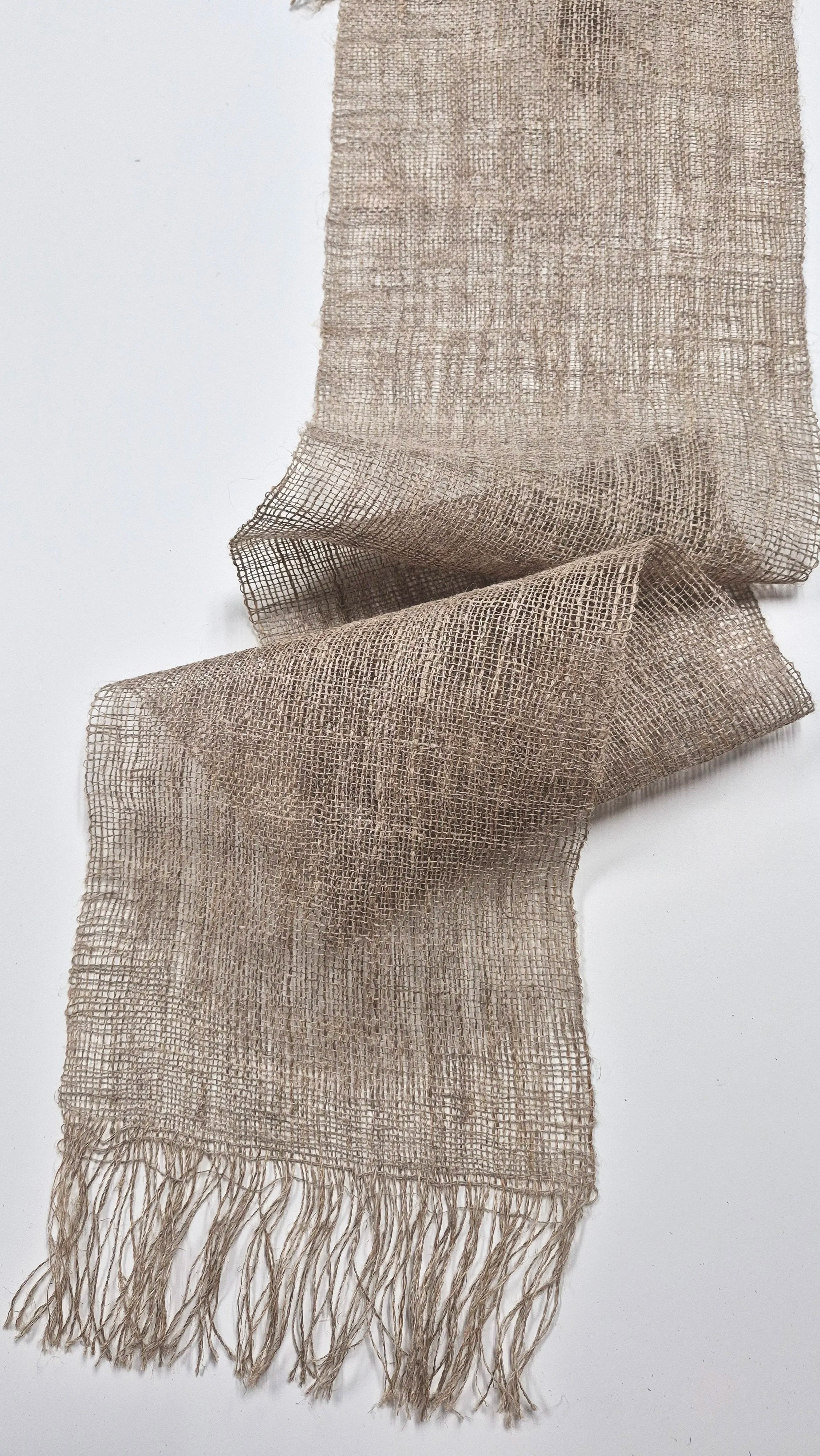 Un foulard en filet beige avec des franges en bas, posé sur un fond blanc.