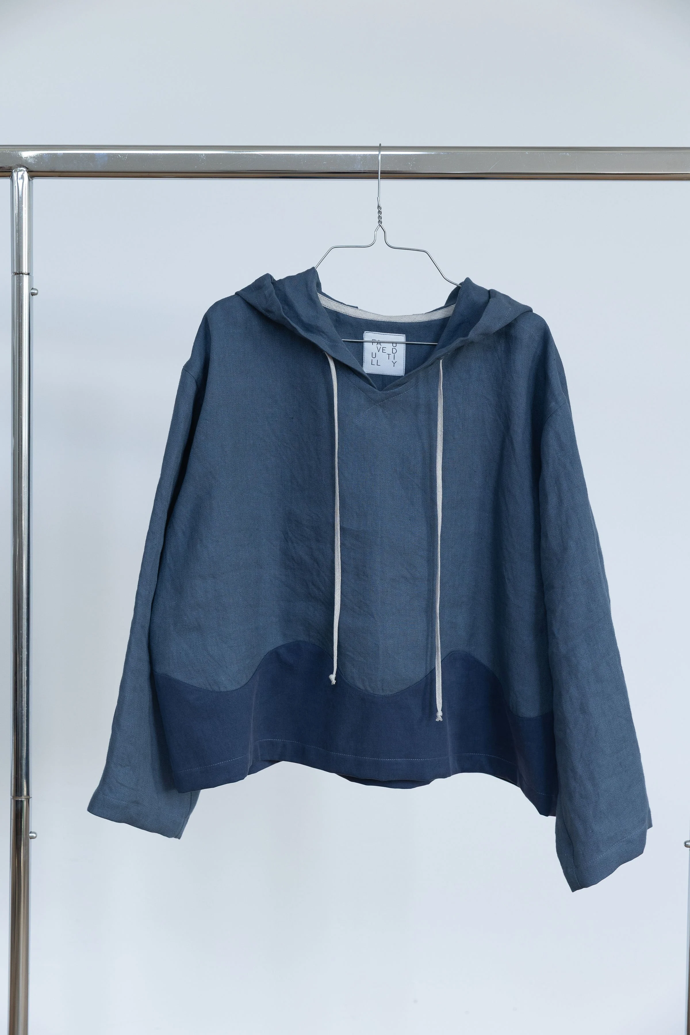 Veste à capuche grise suspendue sur un joli cintre métallique, photo prise en intérieur avec fond blanc.