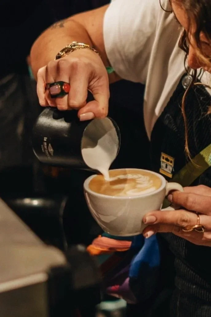 Person pouring steamed milk into a cup of coffee, creating latte art.