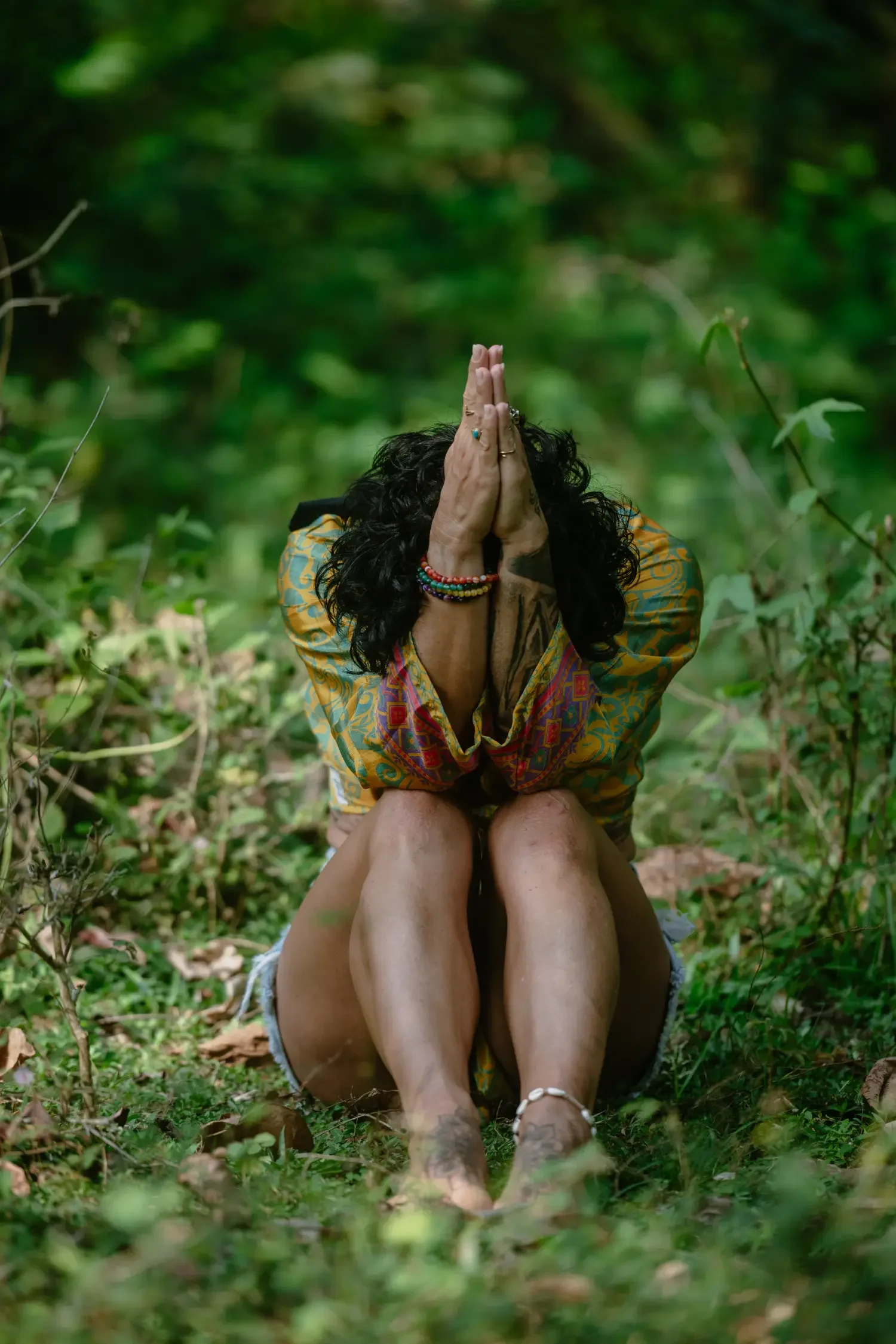 Caro seated in cross-legged meditation with hands in namaste in forest retreat