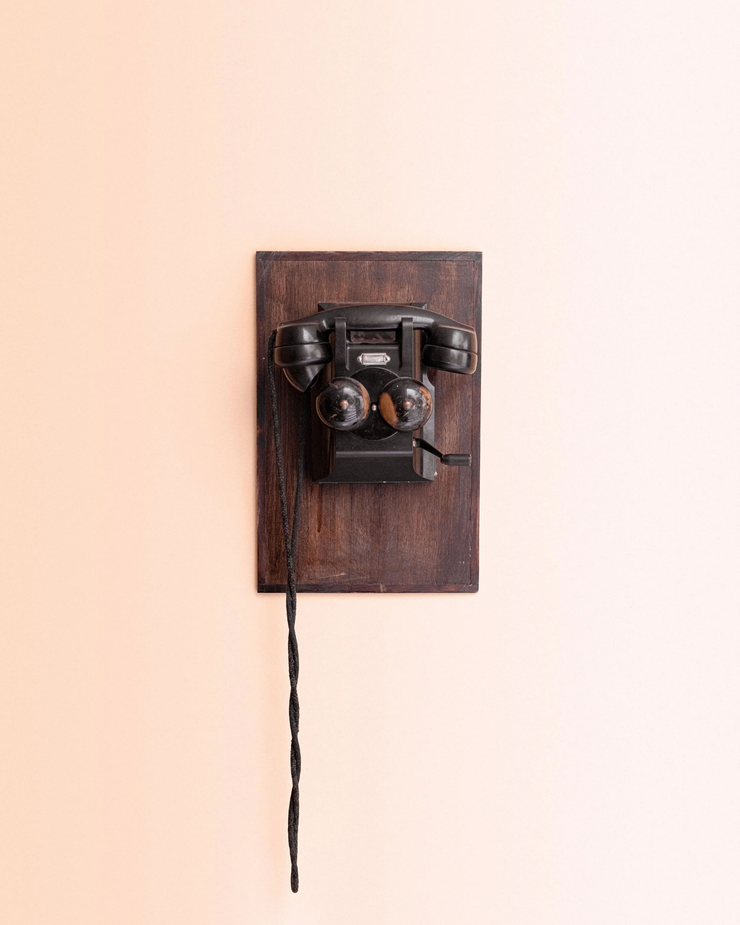 Wall-mounted vintage black rotary telephone with a wooden backplate and a hanging cord.