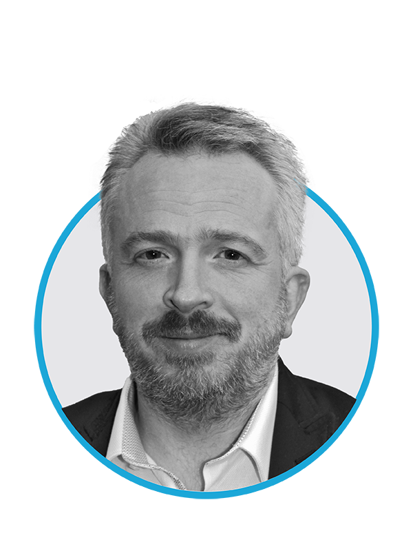 Black and white portrait of middle-aged man with light hair, beard, wearing a collared shirt and blazer, inside a circular frame with a blue border.