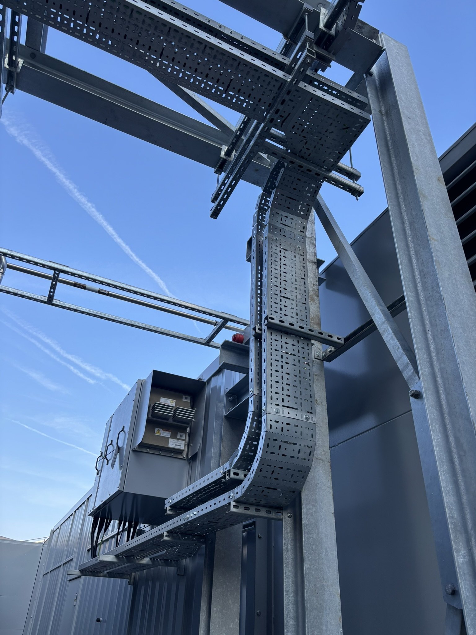 Industrial electrical equipment and cable management system on the exterior of a building, set against a bright blue sky.