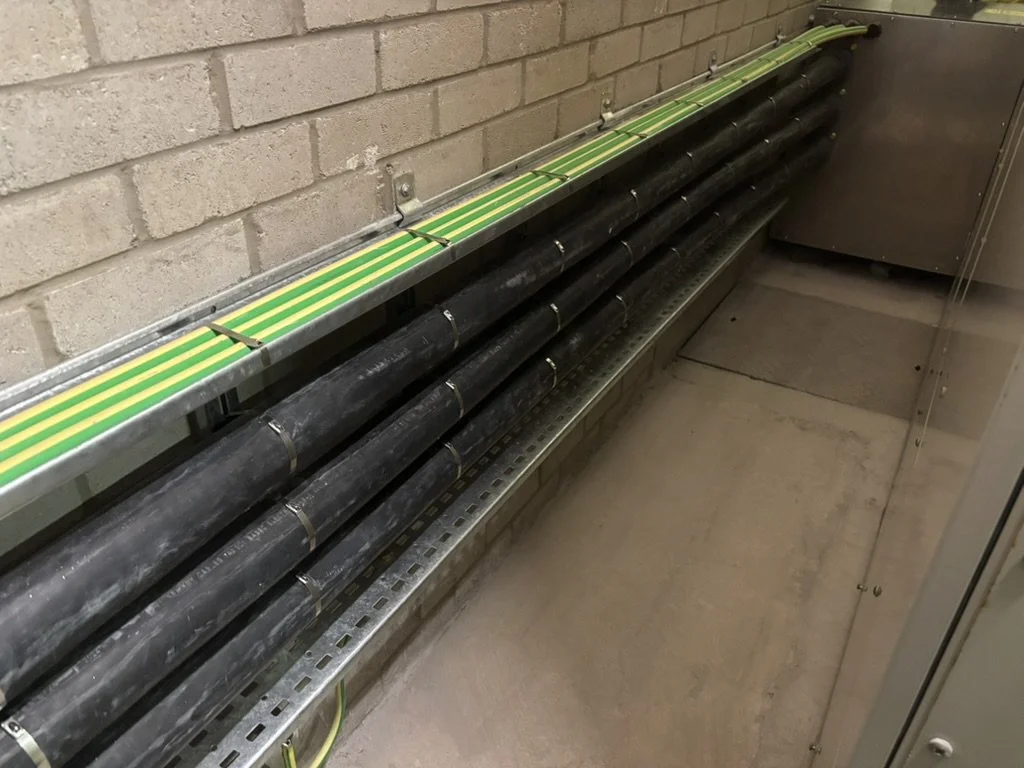 Electrical conduit pipes mounted on a wall with an overhead cable tray, in a utility or electrical room.
