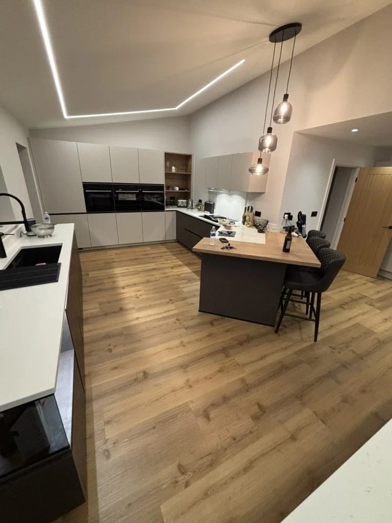 Modern kitchen with white cabinets, a wooden island with black base, and pendant lighting, featuring a wooden floor and minimal decor.