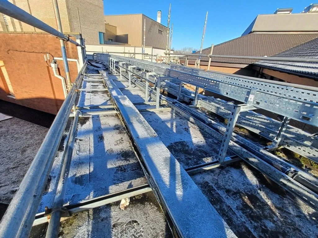 Construction scaffolding and metal framing on a rooftop under a clear blue sky.