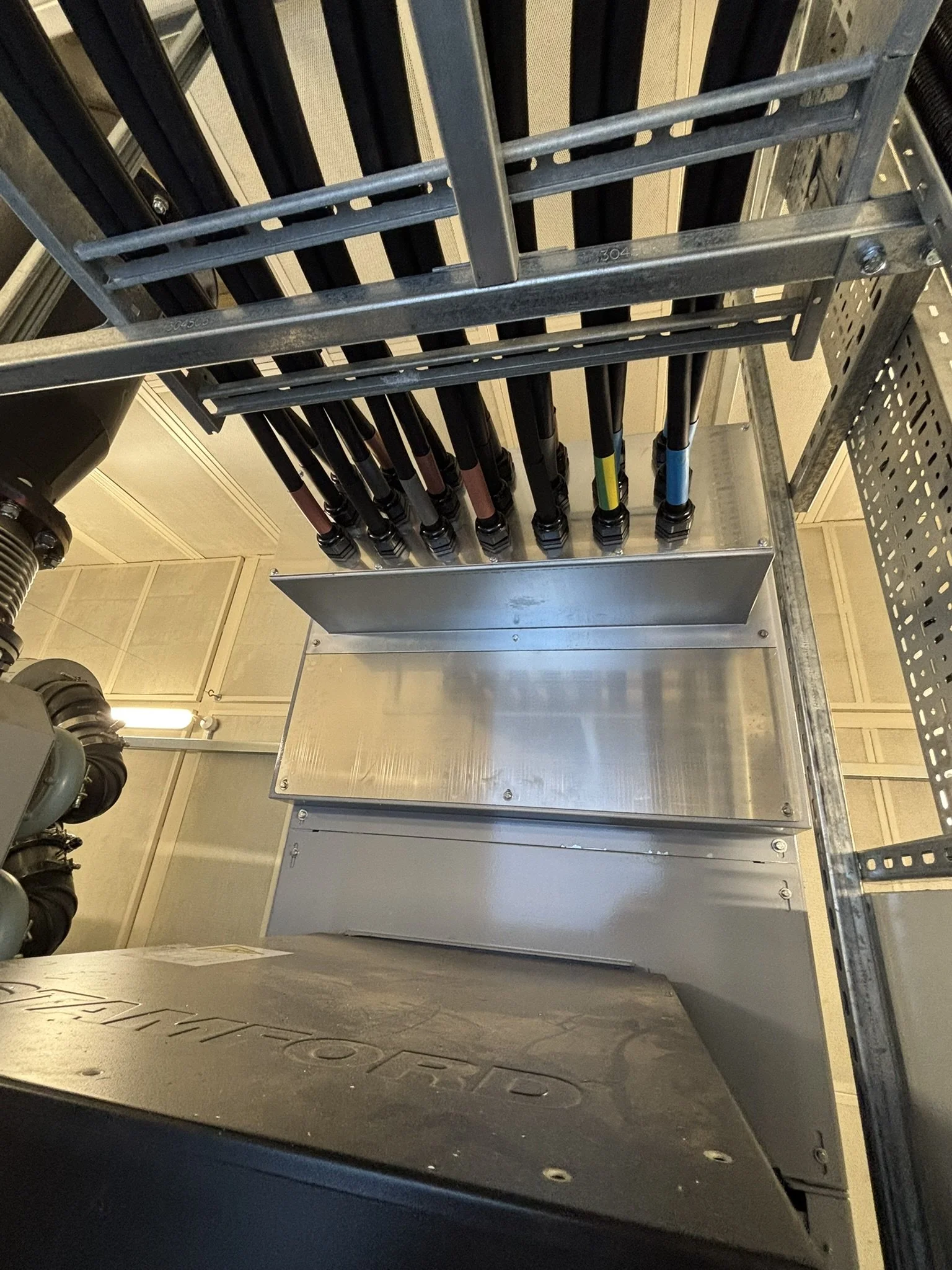 Metal framework with black cables or pipes arranged in parallel, mounted on a metal structure inside an industrial or mechanical room.