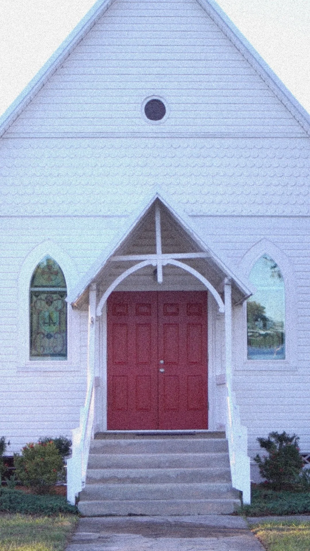 A white church with a red door, arched windows on each side, and a small staircase leading up to the entrance.