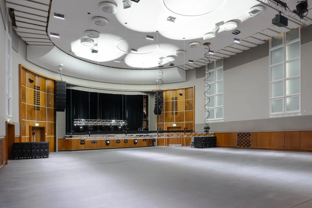 Refurbished performance hall at The Halls Wolverhampton showing stage, technical lighting infrastructure and restored interior finishes.