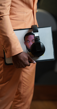 Person holding a tablet with a woman's face on the screen and a pair of headphones resting on it