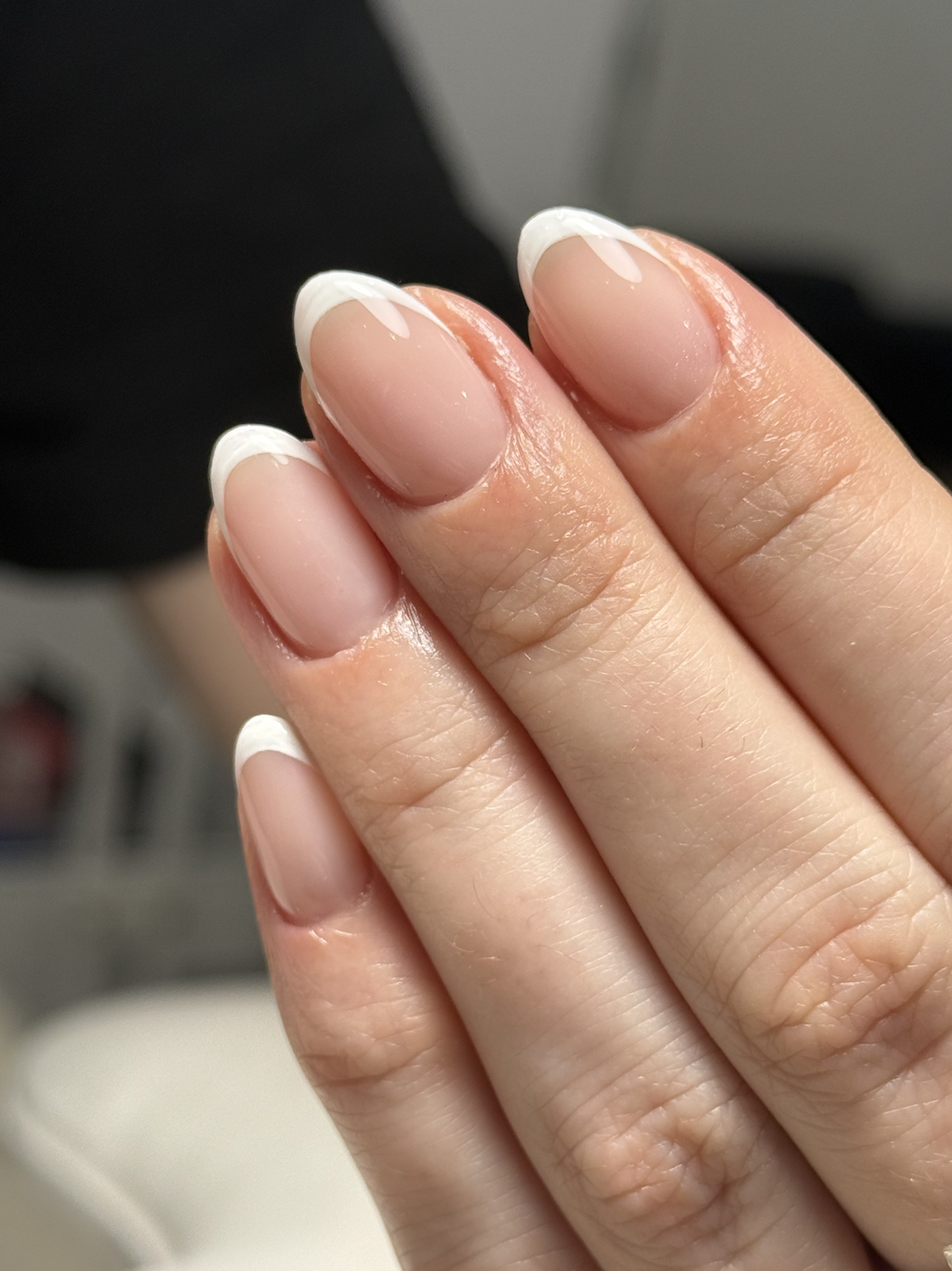 Close-up of a hand with well-manicured nails featuring natural pink color and white tips.