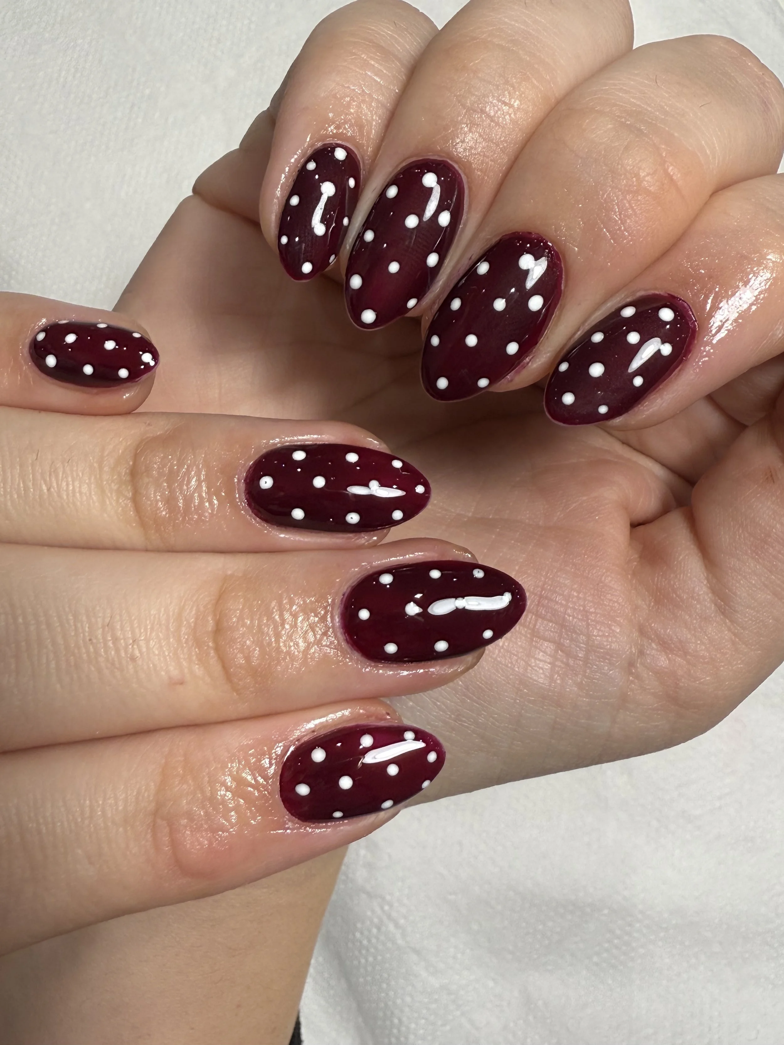 Close-up of a hand with maroon-colored nails decorated with white polka dots.