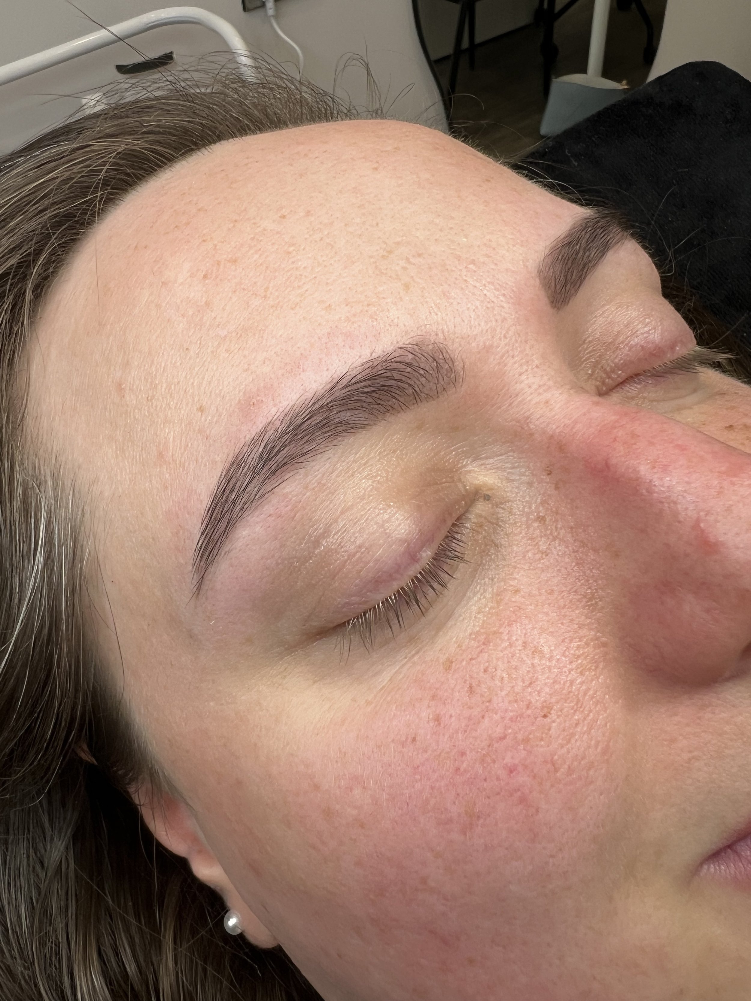 Close-up photograph of a woman's face, showing her closed eye, eyebrow, and part of her forehead and cheek. Her skin appears clear and smooth, with natural texture and a slight redness on her cheek.