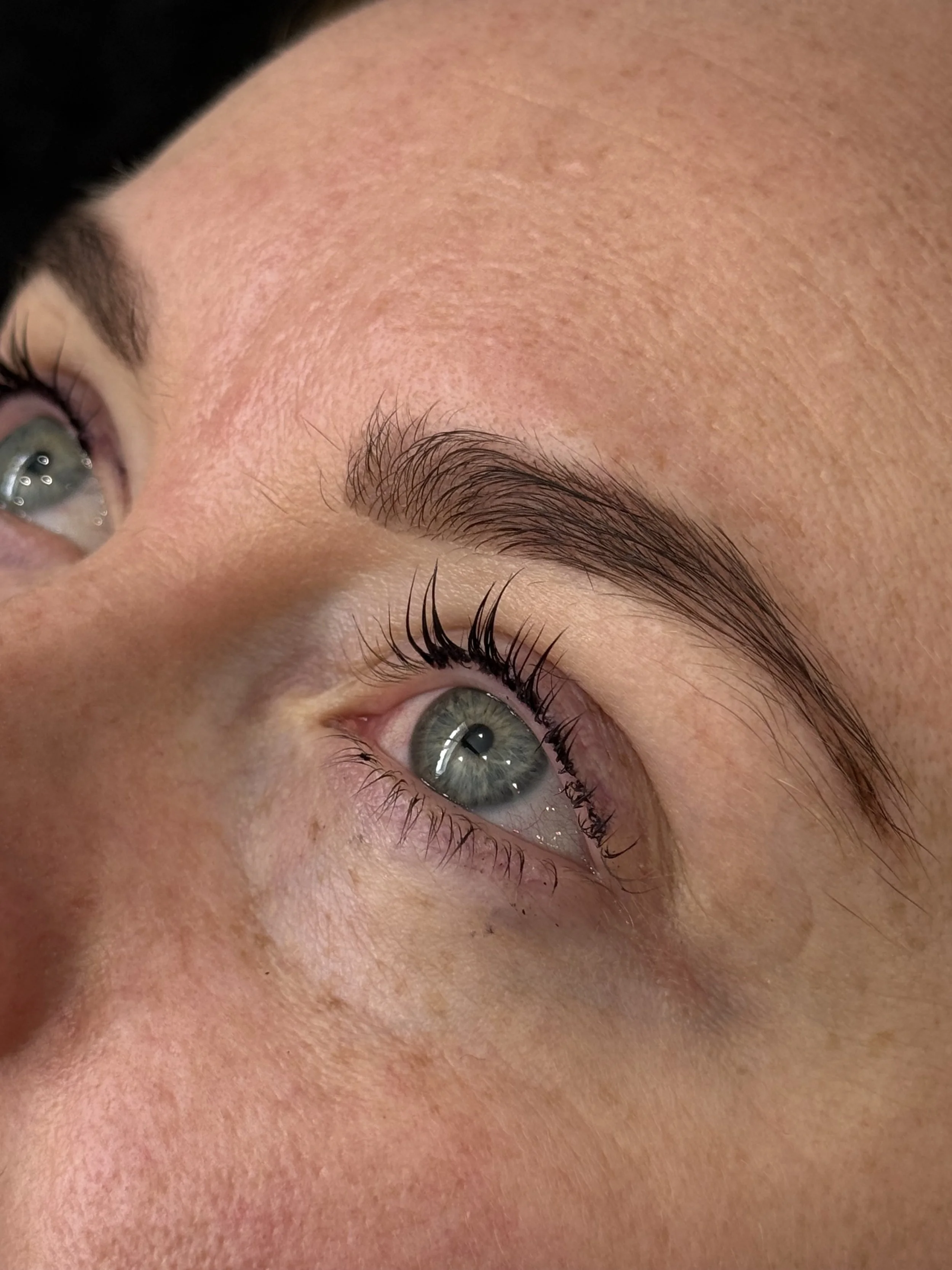 Close-up of a person's eye, eye makeup, and eyebrow, showing the skin texture and eyelashes.
