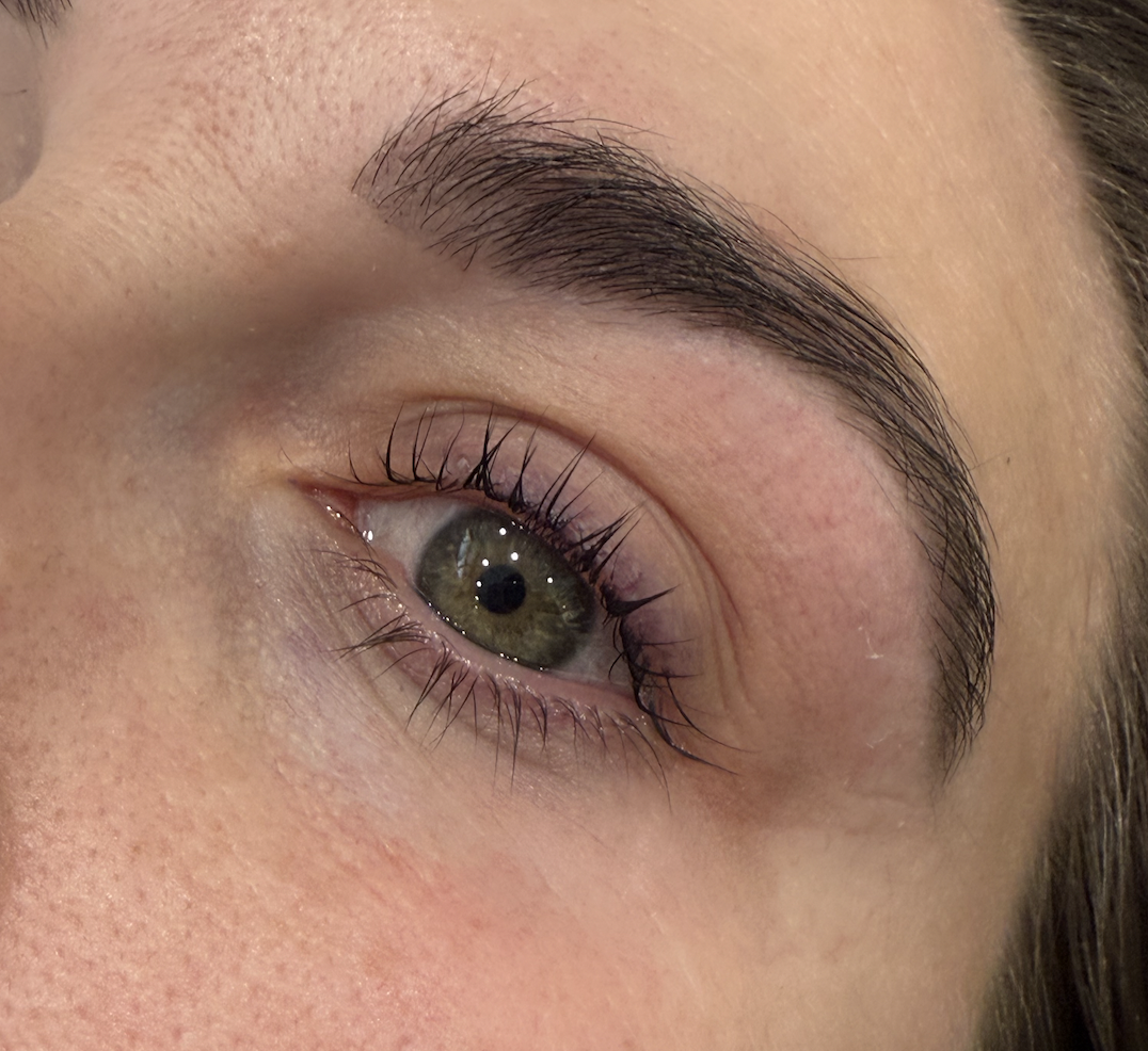 Close-up of a woman's eye, showing detailed eyelashes, brown eyebrow, and hazel-green iris.
